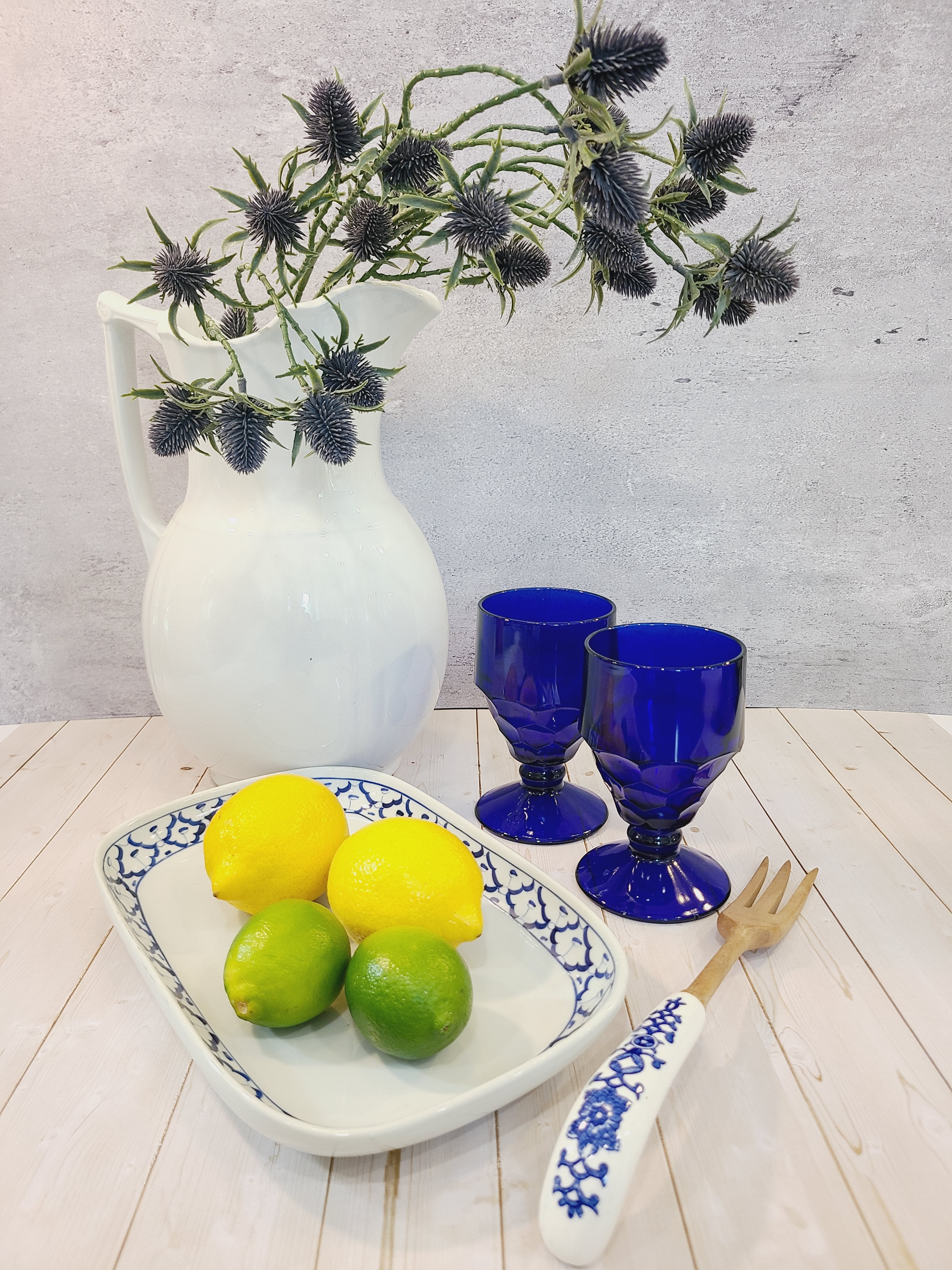 Antique white Alfred Meakin Royal Ironstone Pitcher styled with cobalt blue goblets, blue and white platter holding lemons, wooden fork with ceramic handle.