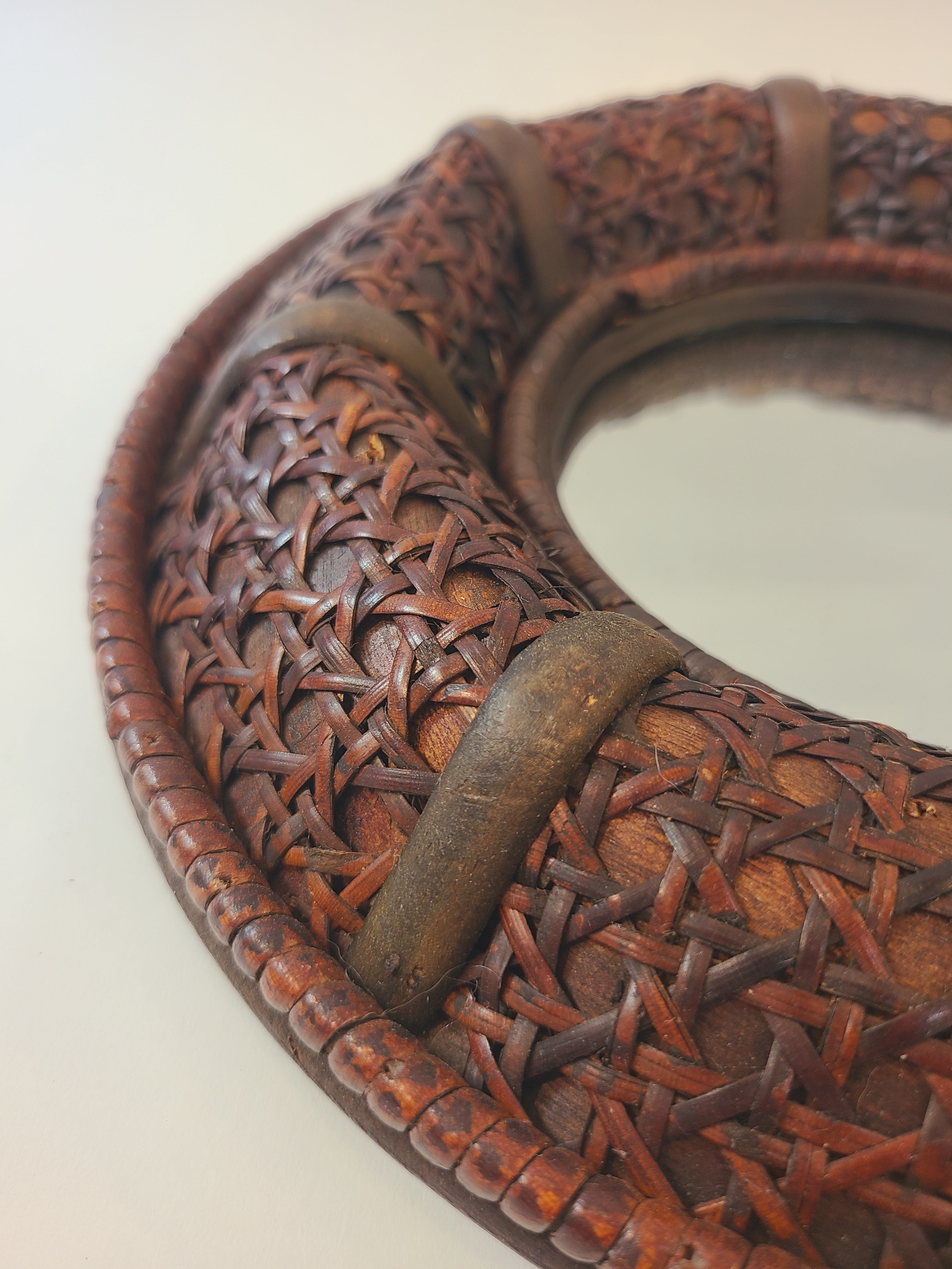Close up of the dark brown cane frame of vintage round wall mirror.
