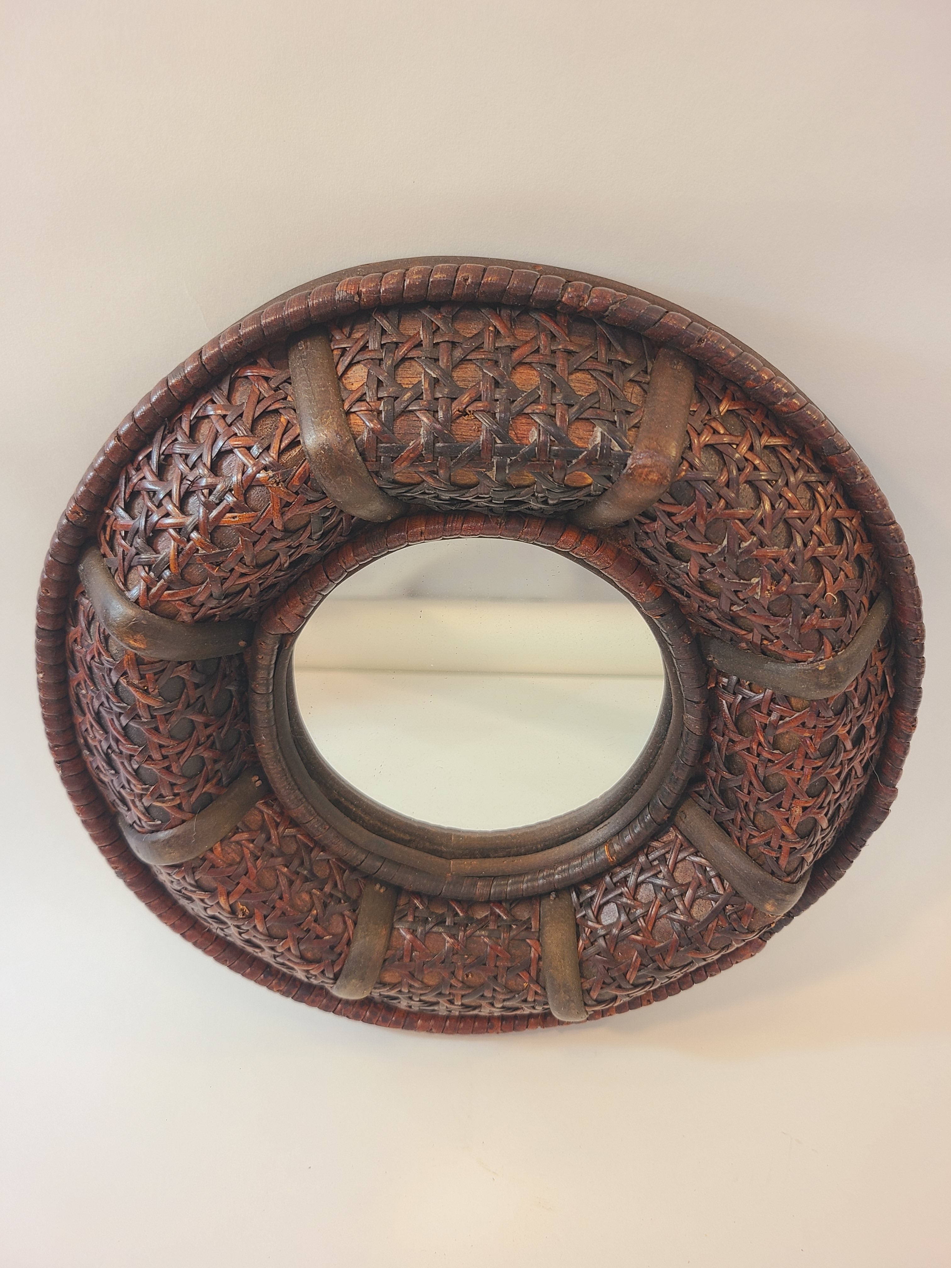 A vintage round wall mirror with an intricate dark brown cane frame.