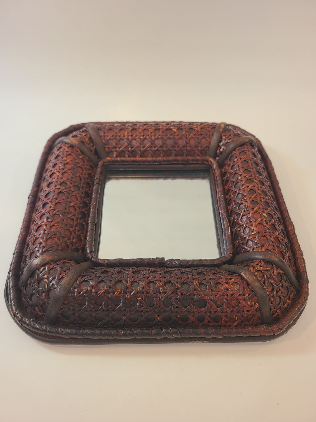 A vintage square decorative wall mirror with an intricately woven dark brown cane frame.