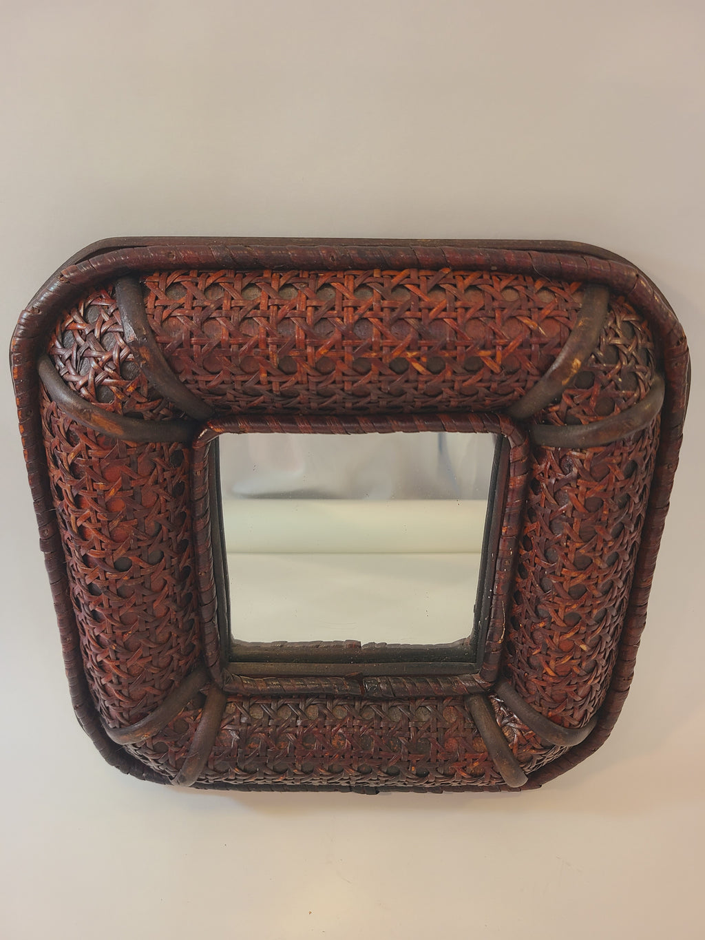 A vintage square decorative wall mirror with an intricately woven dark brown cane frame, photographed against a plain light background.