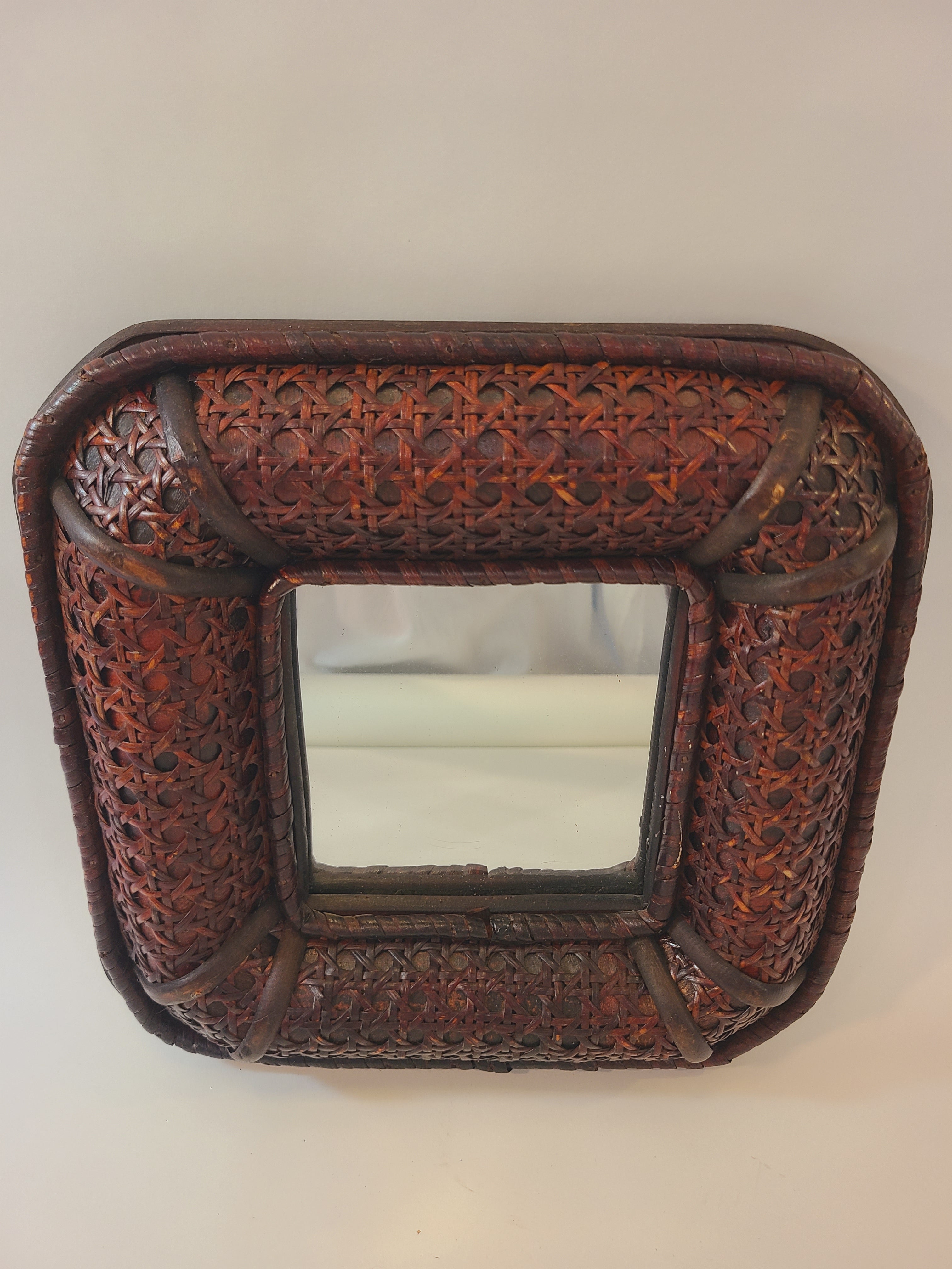 A vintage square decorative wall mirror with an intricately woven dark brown cane frame, photographed against a plain light background.
