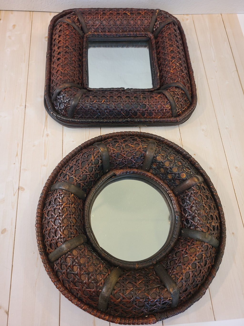 A vintage round wall mirror with an intricate dark brown cane frame photographed with a matching square mirror.