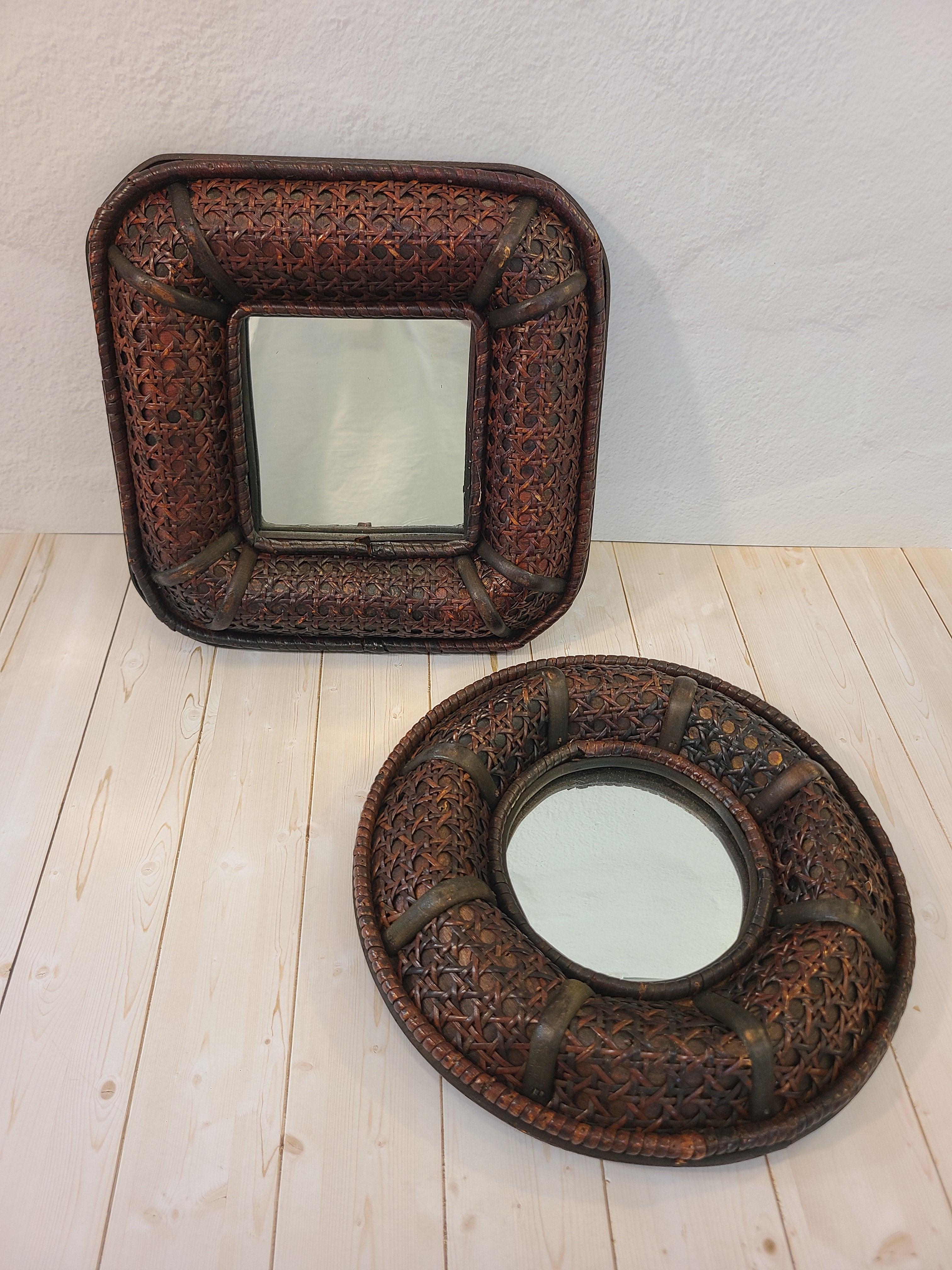A vintage round wall mirror with an intricate dark brown cane frame shown against a light wood background with a companion square mirror.