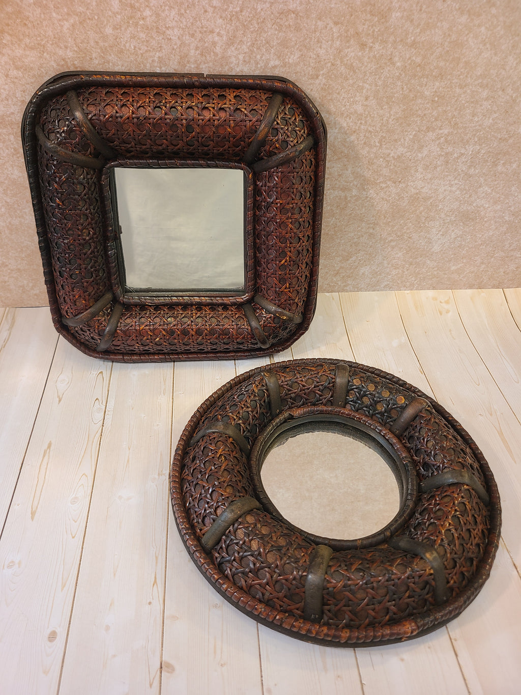 A vintage square decorative wall mirror with an intricately woven dark brown cane frame, photographed with a matching round mirror.