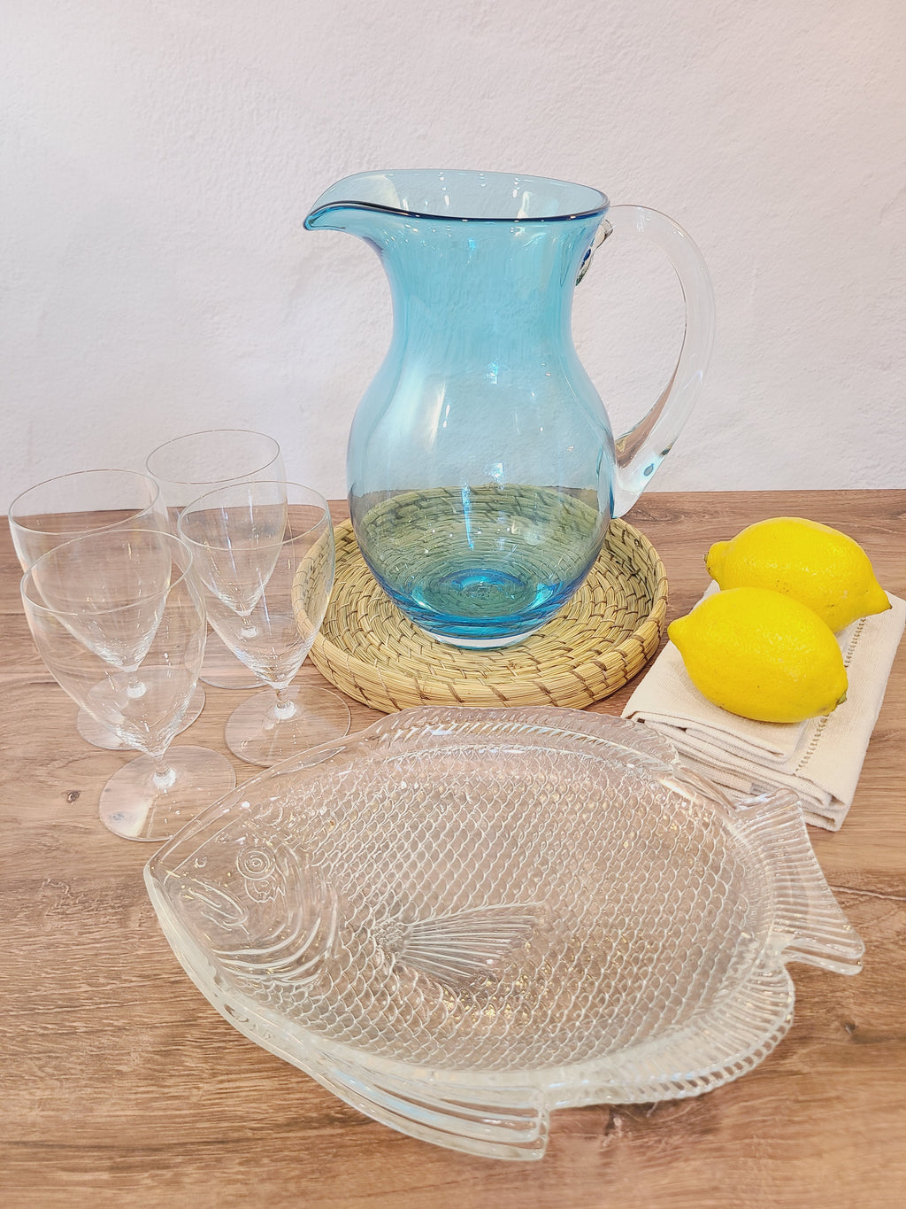 Turquoise glass vase with clear glass handle displayed with clear glasses, fish plates, and lemons.