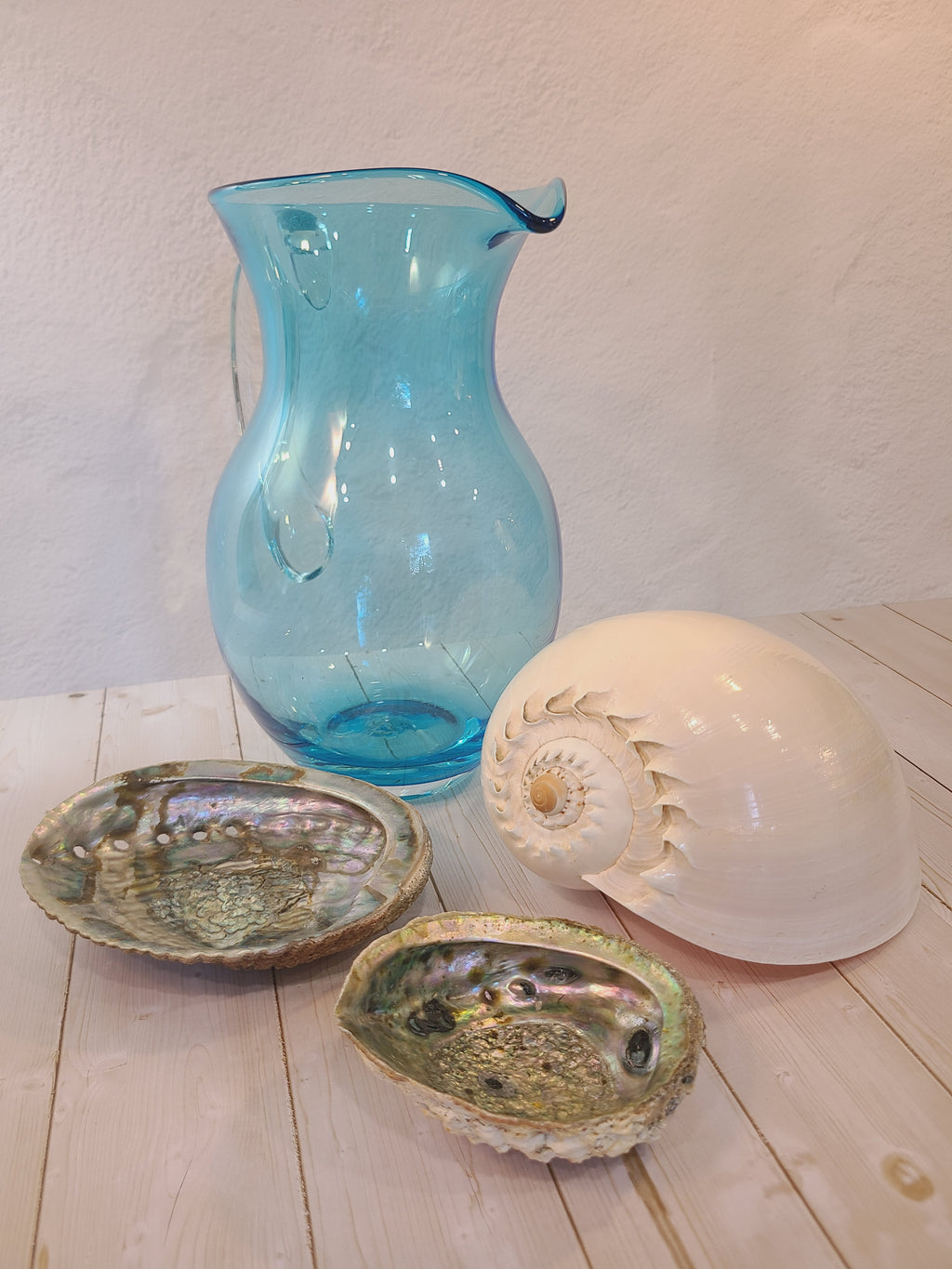 Turquoise glass vase with clear glass handle displayed with shells.