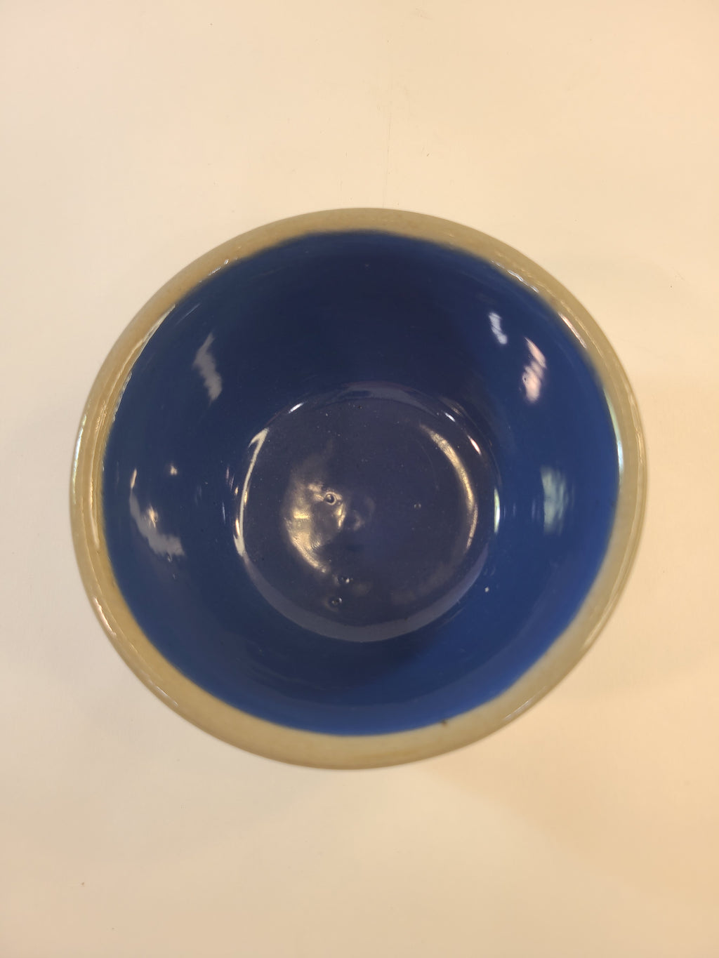 A top-down view of a vintage crock with a glossy deep blue interior and gray rim, set against a plain off-white background.