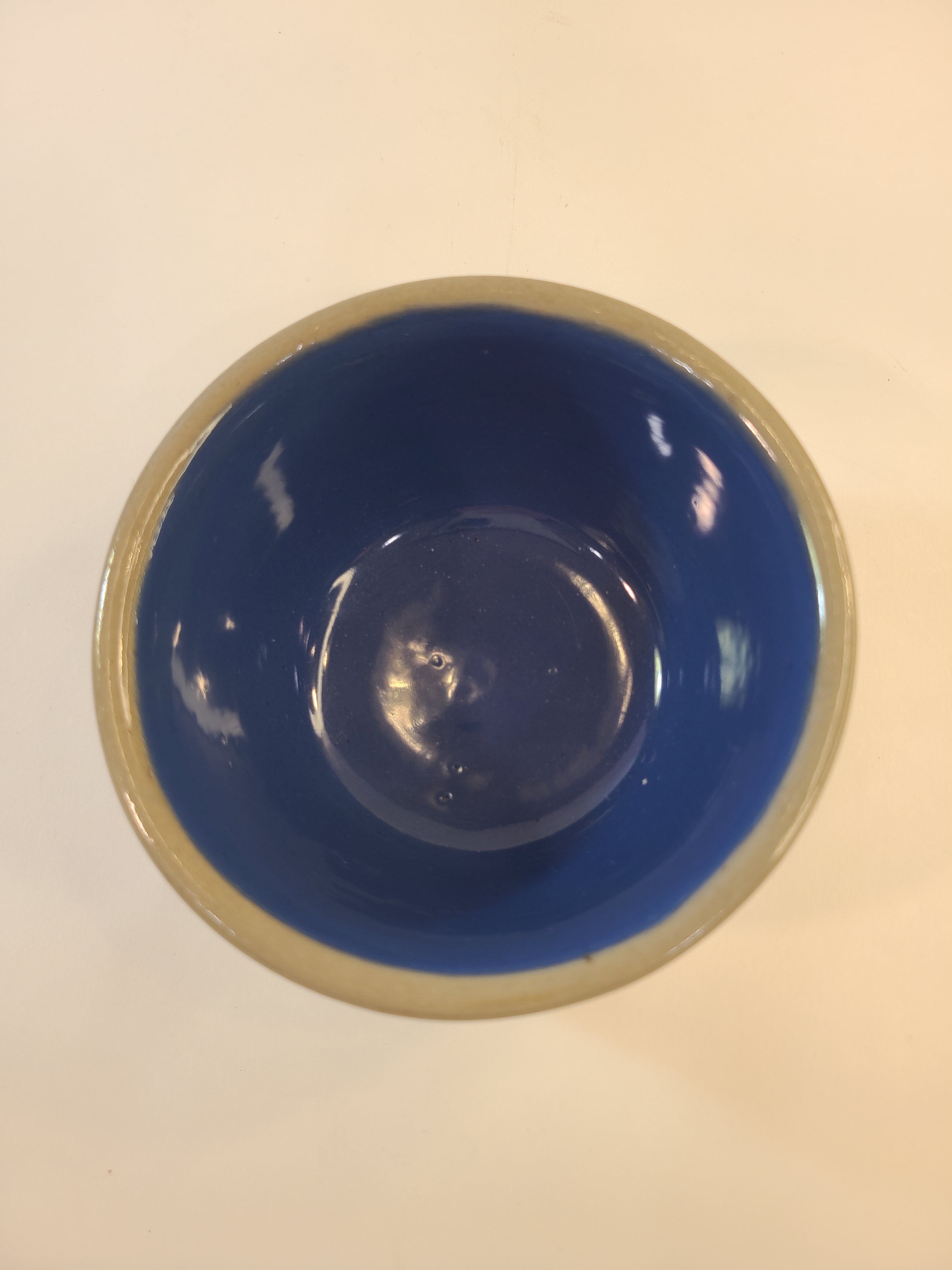 A top-down view of a vintage crock with a glossy deep blue interior and gray rim, set against a plain off-white background.