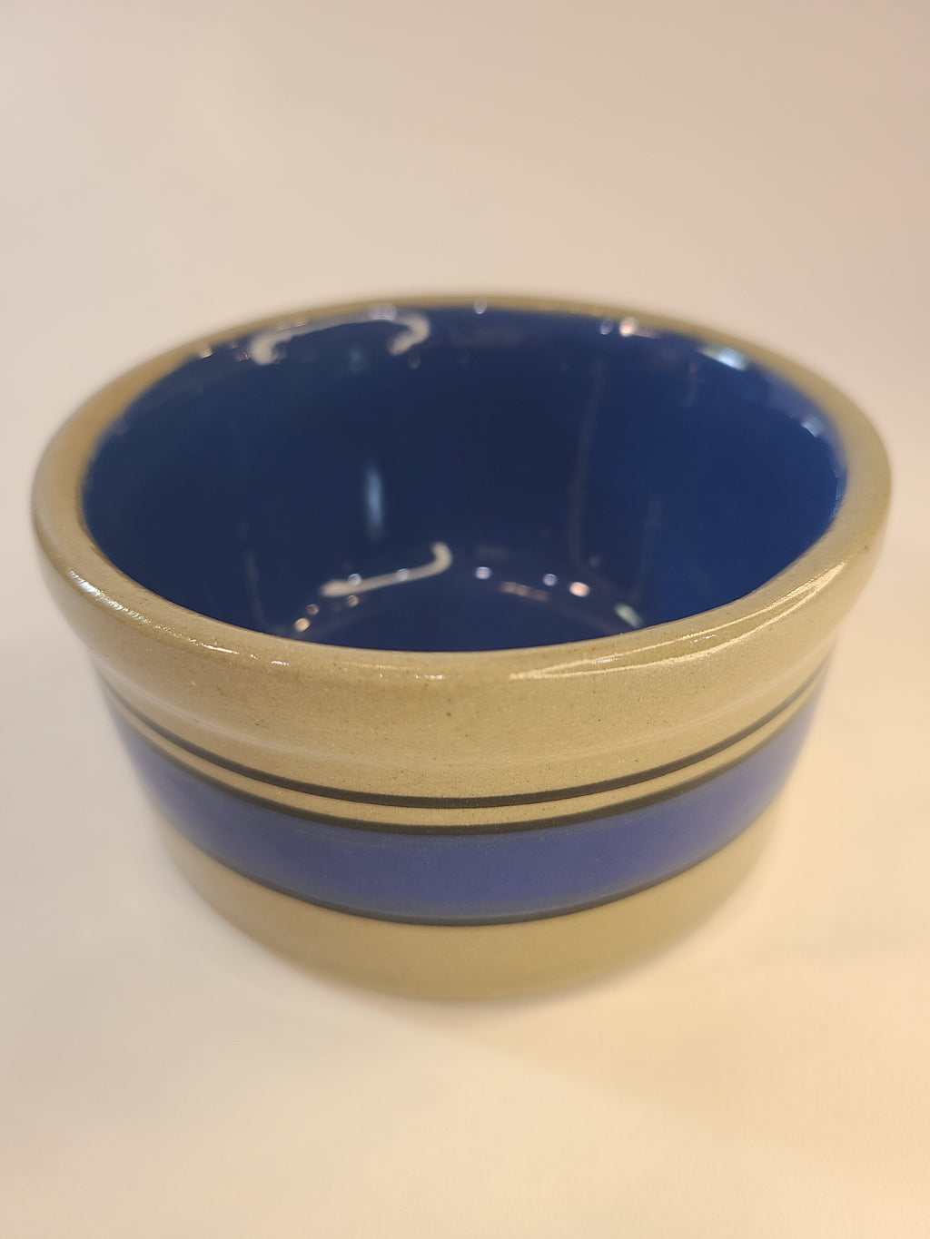 A small vintage stoneware crock with a deep blue interior and gray exterior accented by horizontal blue stripes.
