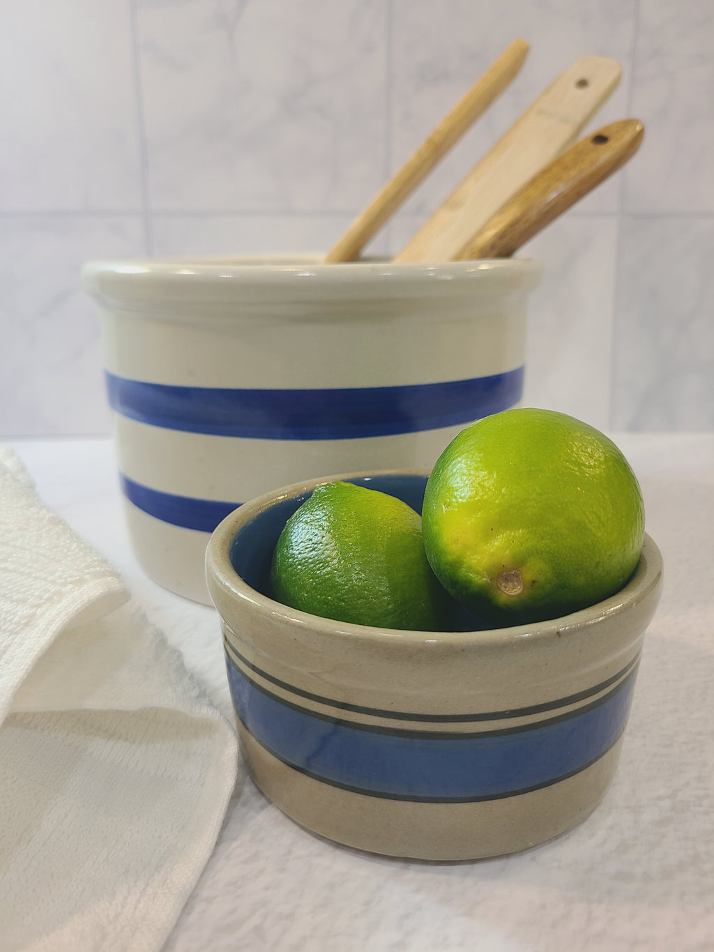 Petite vintage gray crock with blue stripes holding limes with larger crock in background.