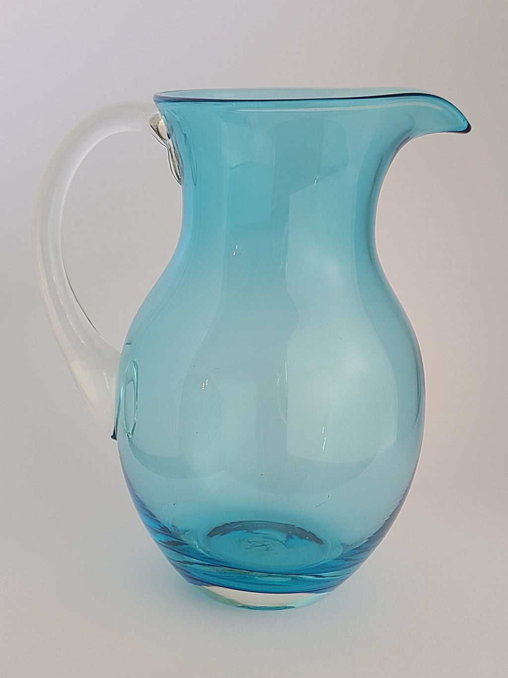 Side view of Turquoise glass vase with clear glass handle on light background.