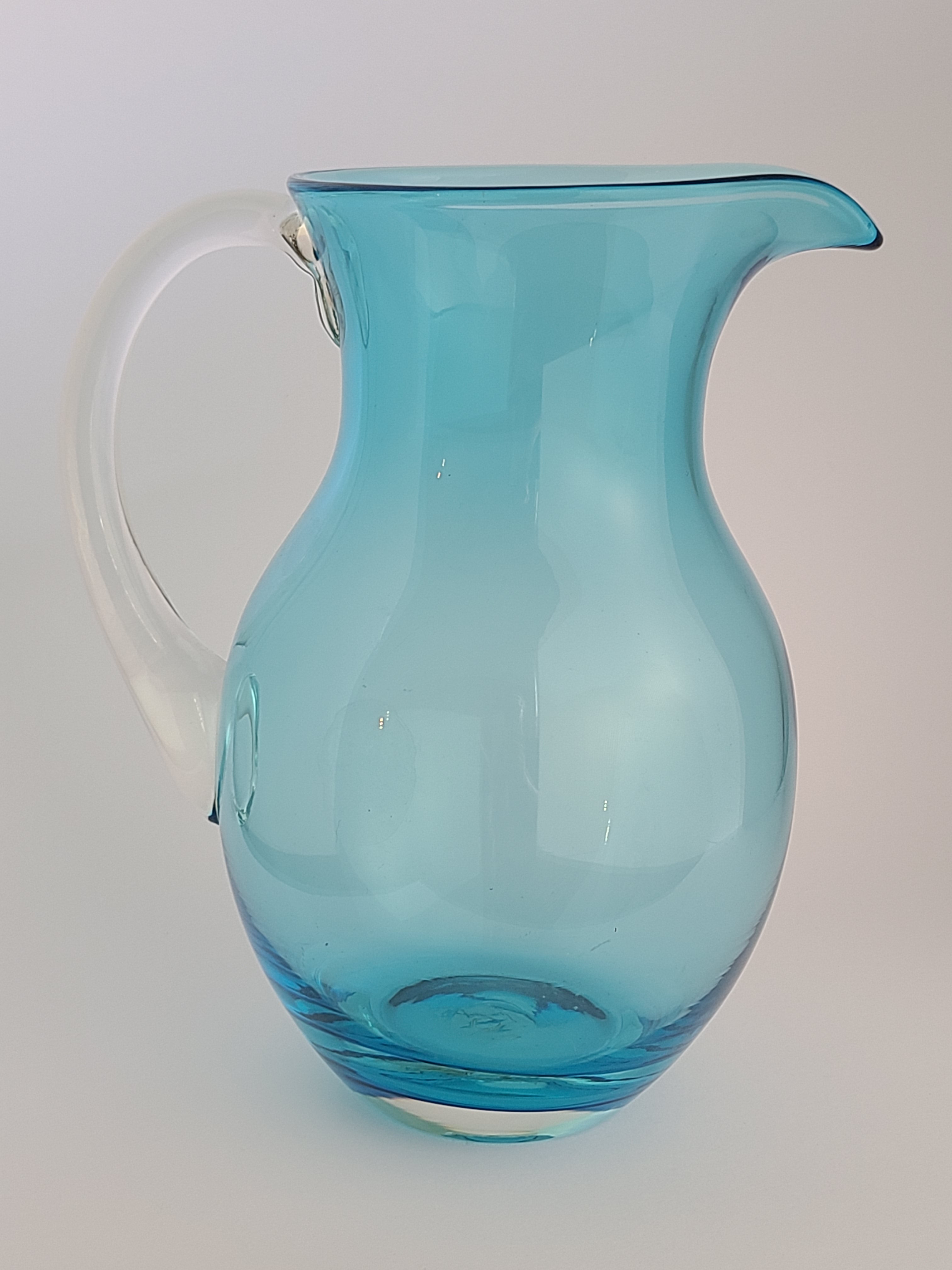 Side view of Turquoise glass vase with clear glass handle on light background.