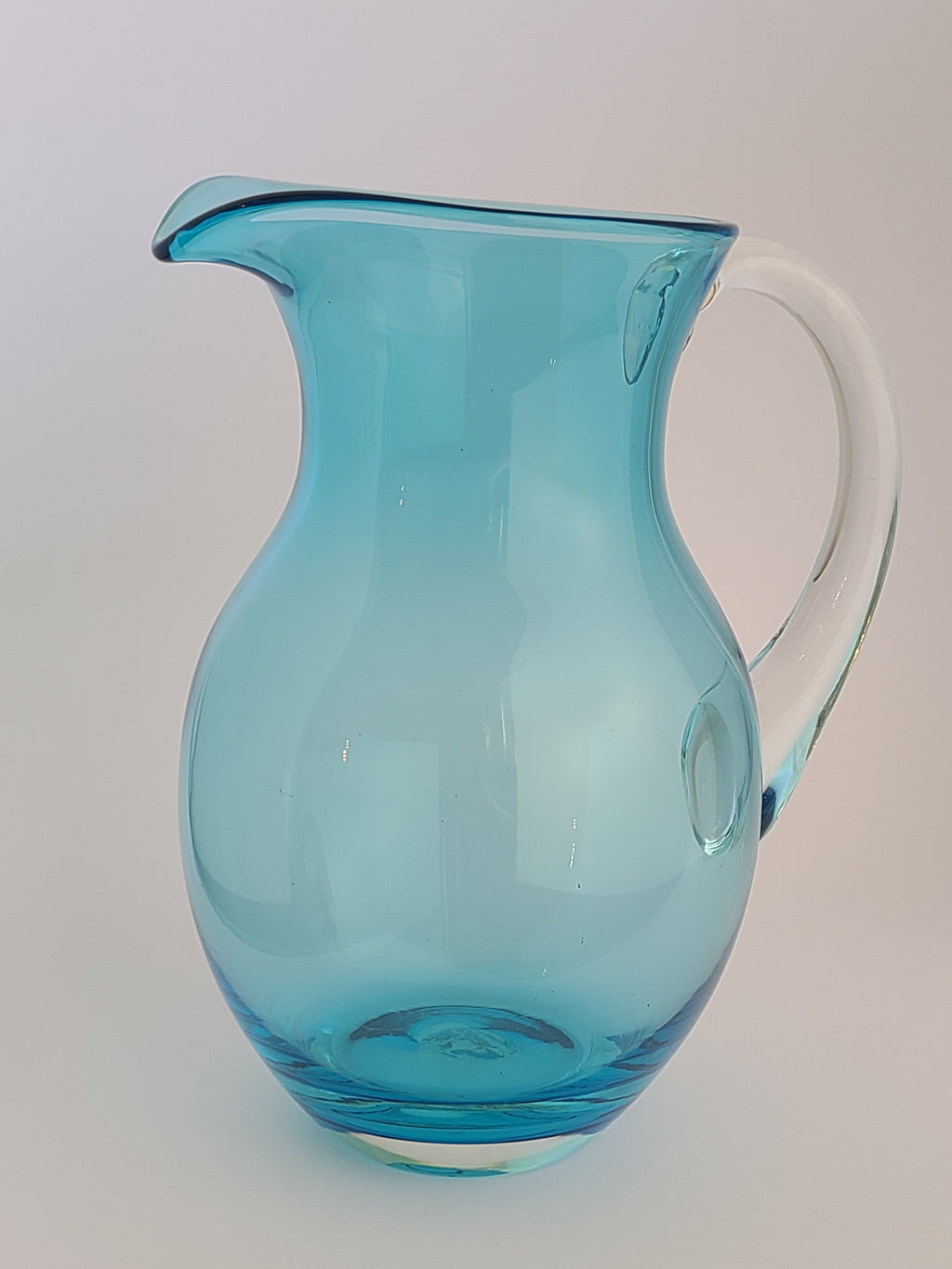Turquoise glass vase with clear glass handle against light background.