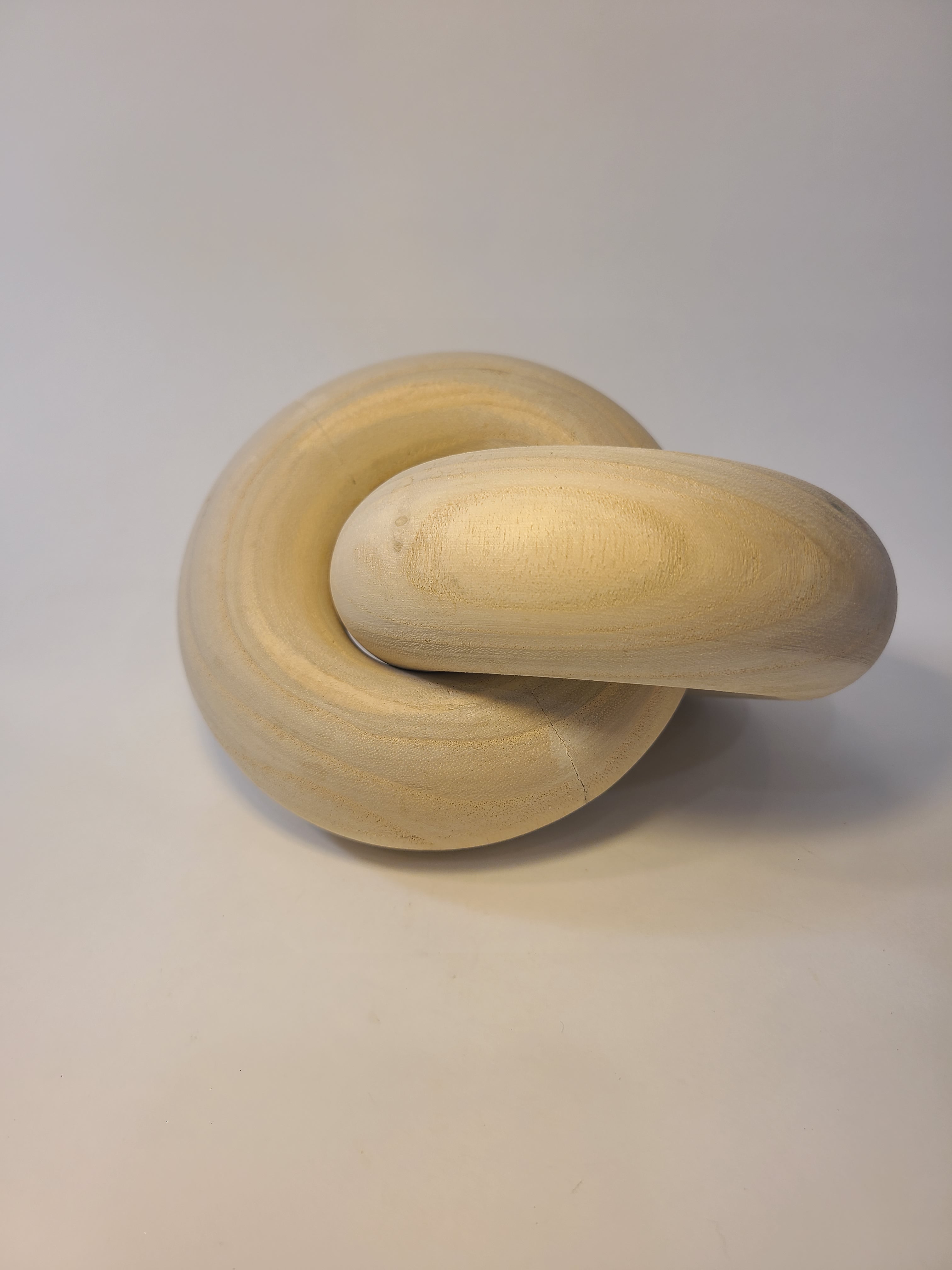 Light natural wood interlocking rings with a smooth surface photographed on a neutral background.
