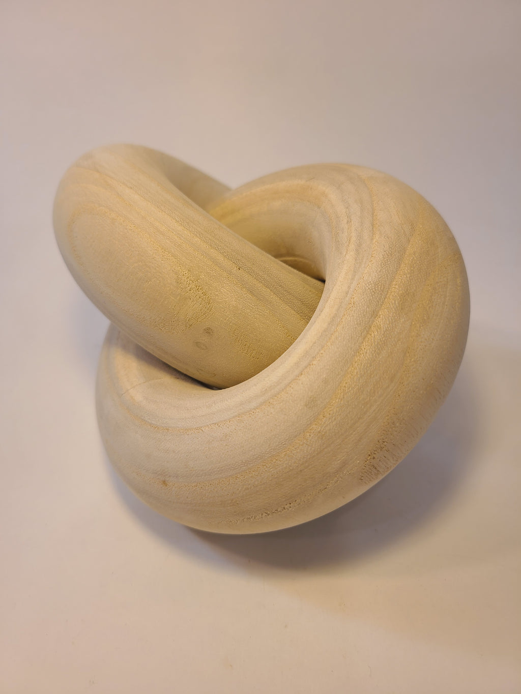 A light natural wood interlocking rings decoration photographed on a plain light beige background.