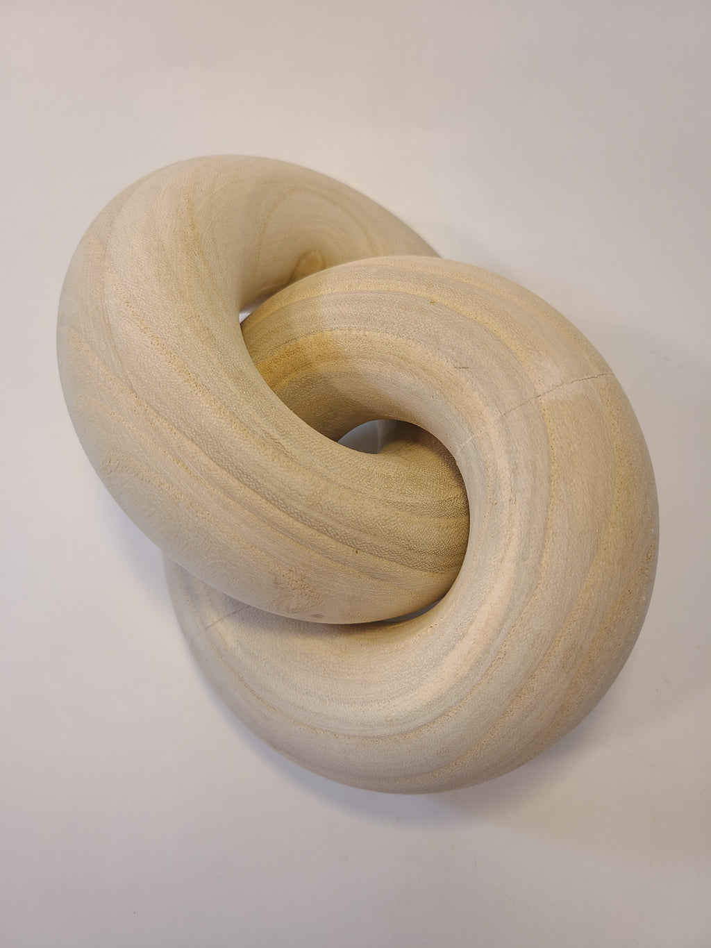 A light natural wood interlocking knot decorative object, photographed on a plain background.