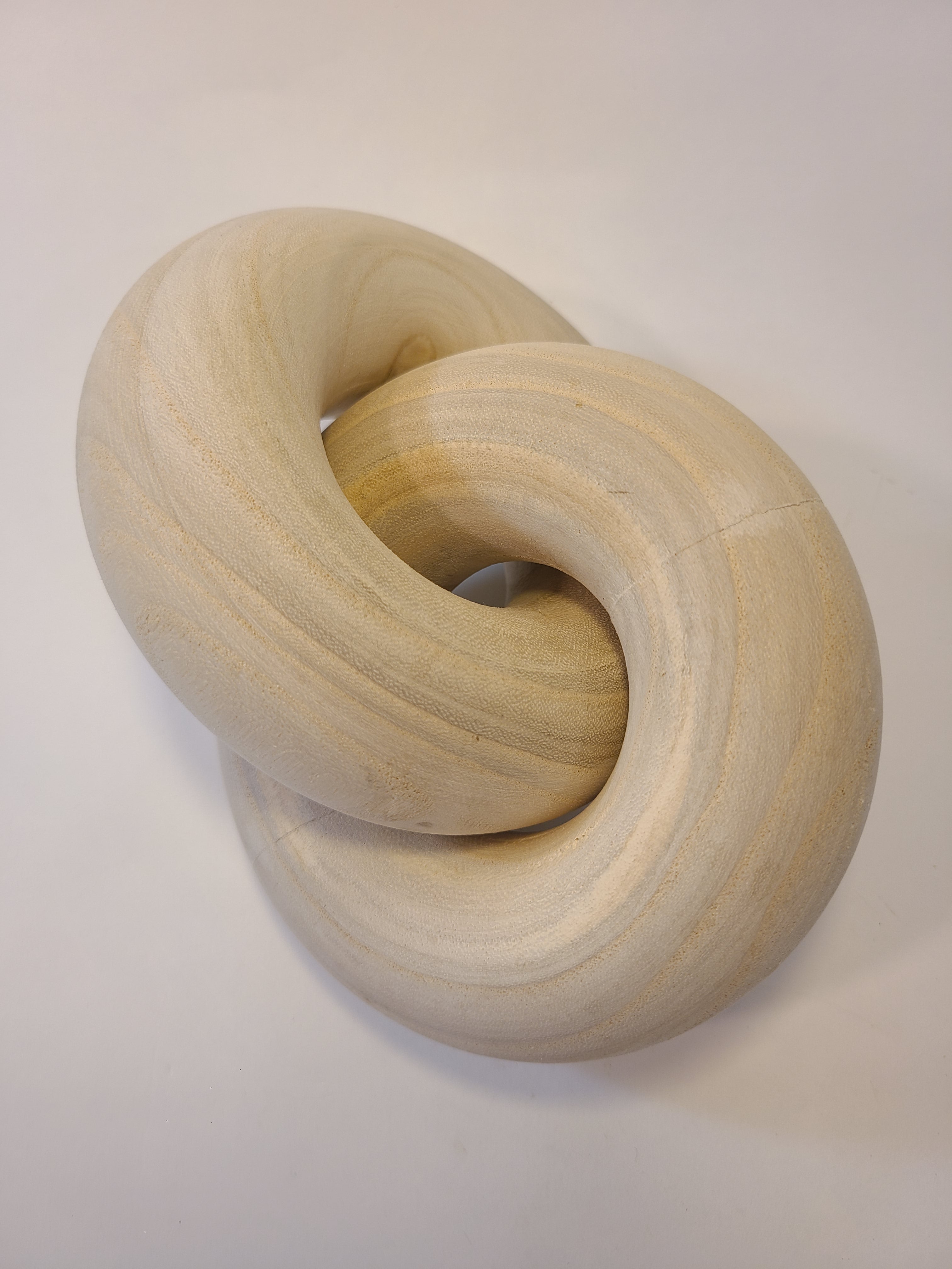 A light natural wood interlocking knot decorative object, photographed on a plain background.
