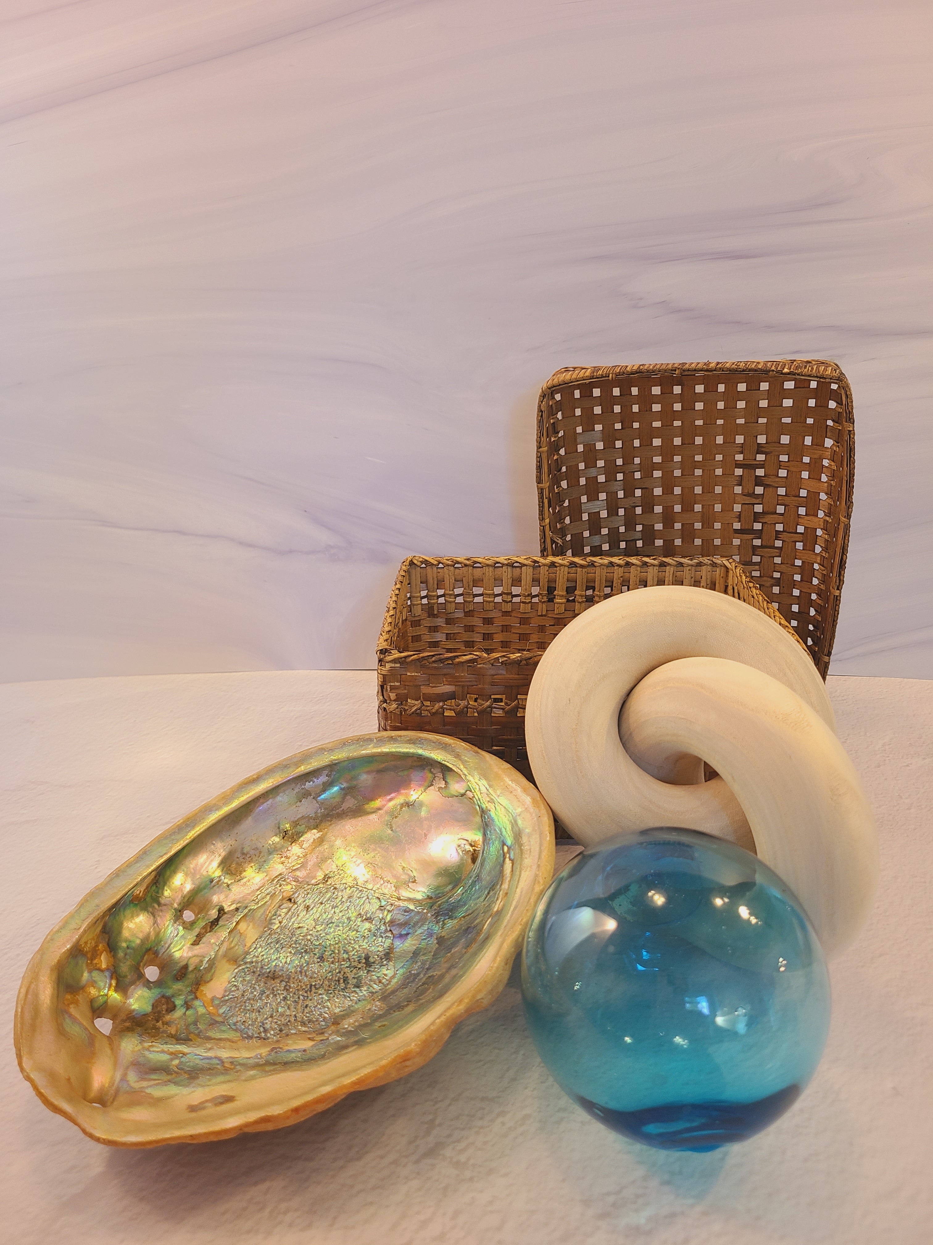 A collection of decorative home decor items including a basket, glass fishing floats, a seashell, and wooden interlocking rings.