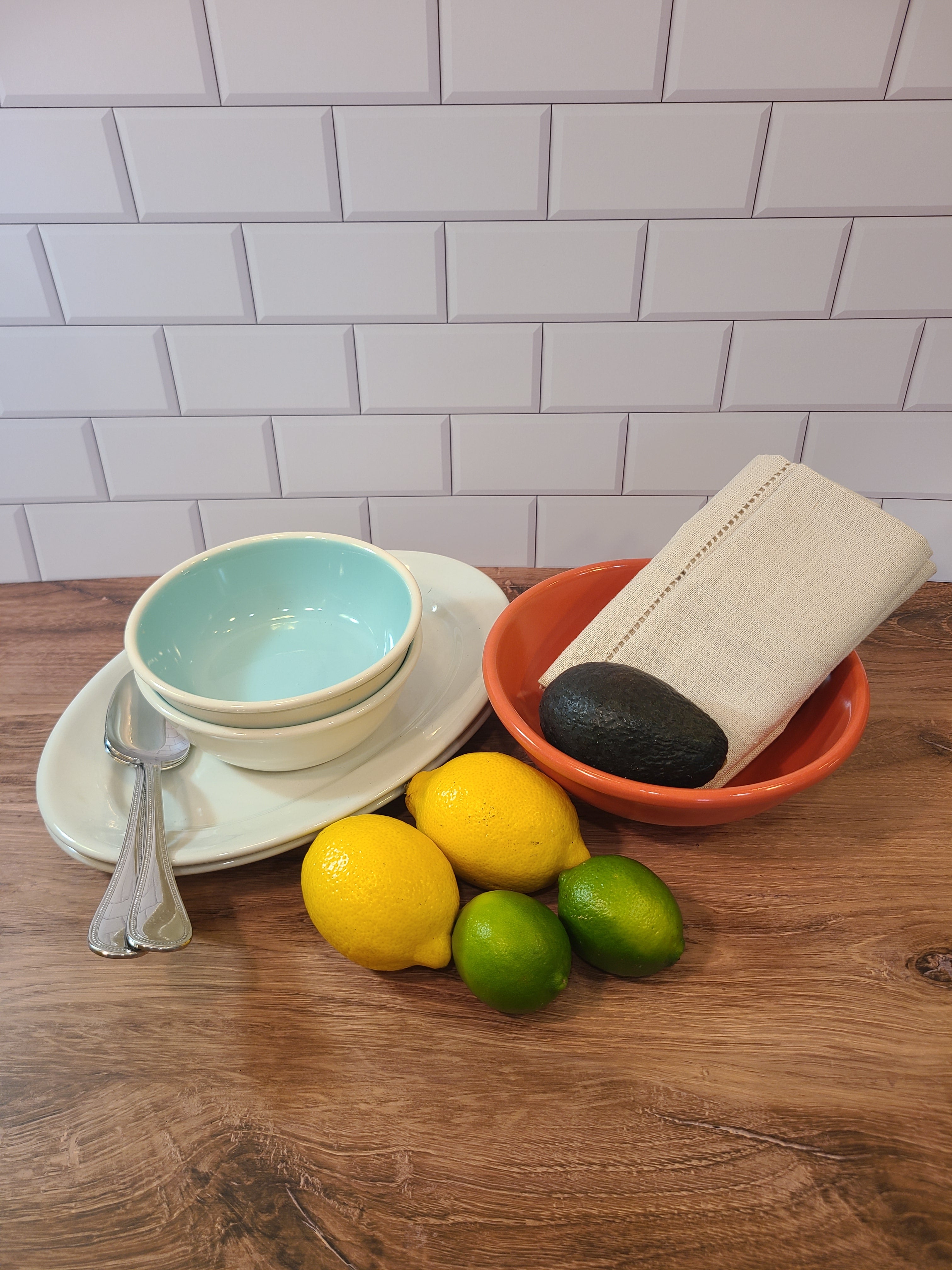 Overhead view of Two vintage Chateau Buffet Stoneware Bowls with turquoise interior and white exterior styled with citrus fruit, avocado, silverware, coral colored bowl, and linen napkins.