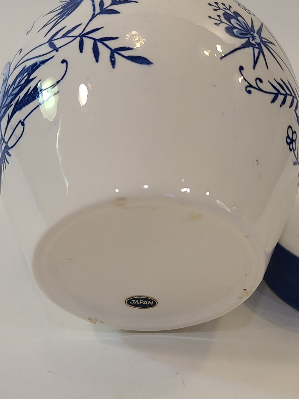A vintage Japanese white ceramic tea jar with a blue floral hand-painted pattern and a blue and white lid showing a Japan label on the bottom.