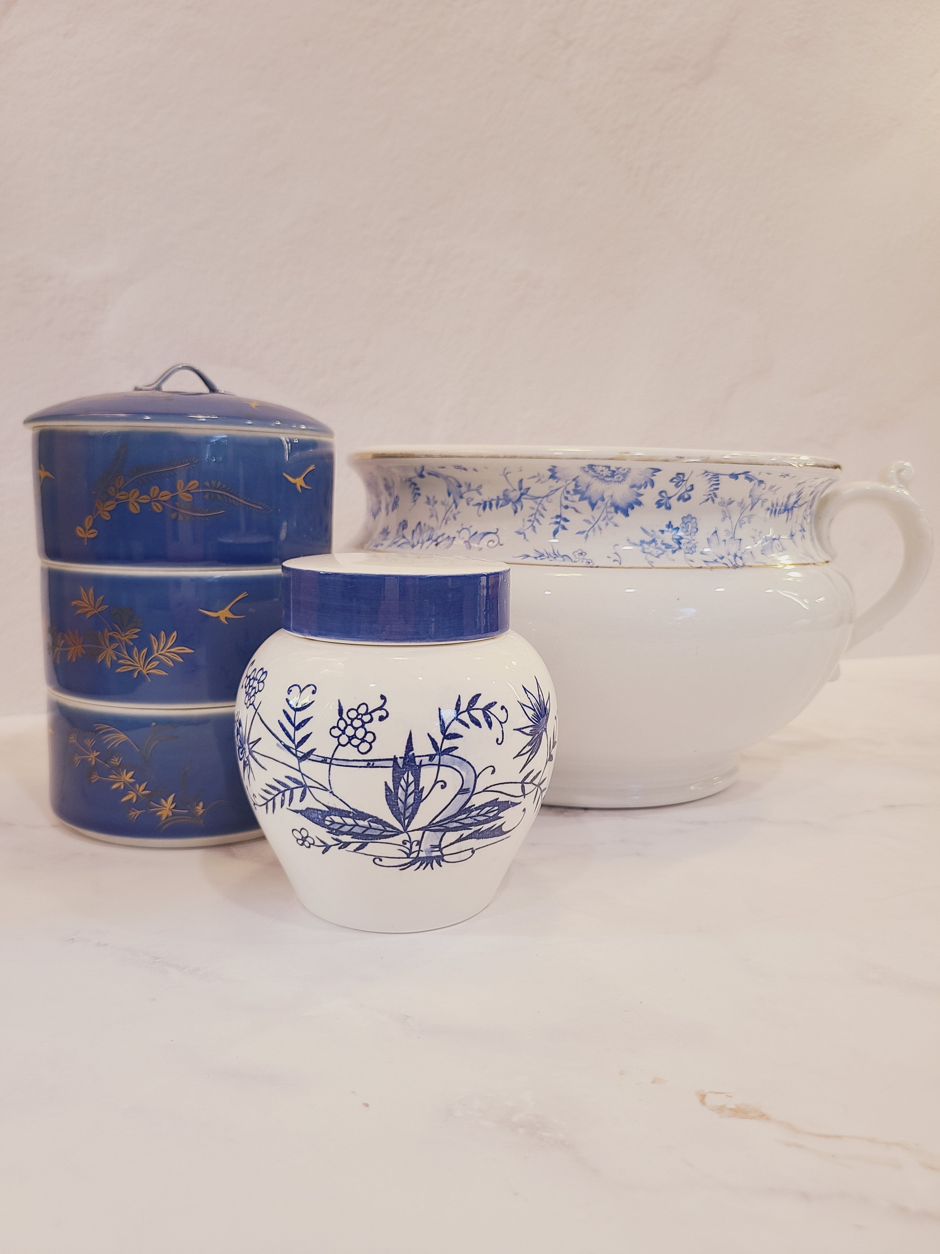 A vintage Japanese white ceramic tea jar with a blue floral hand-painted pattern and a blue and white lid displayed with other ceramic pieces.