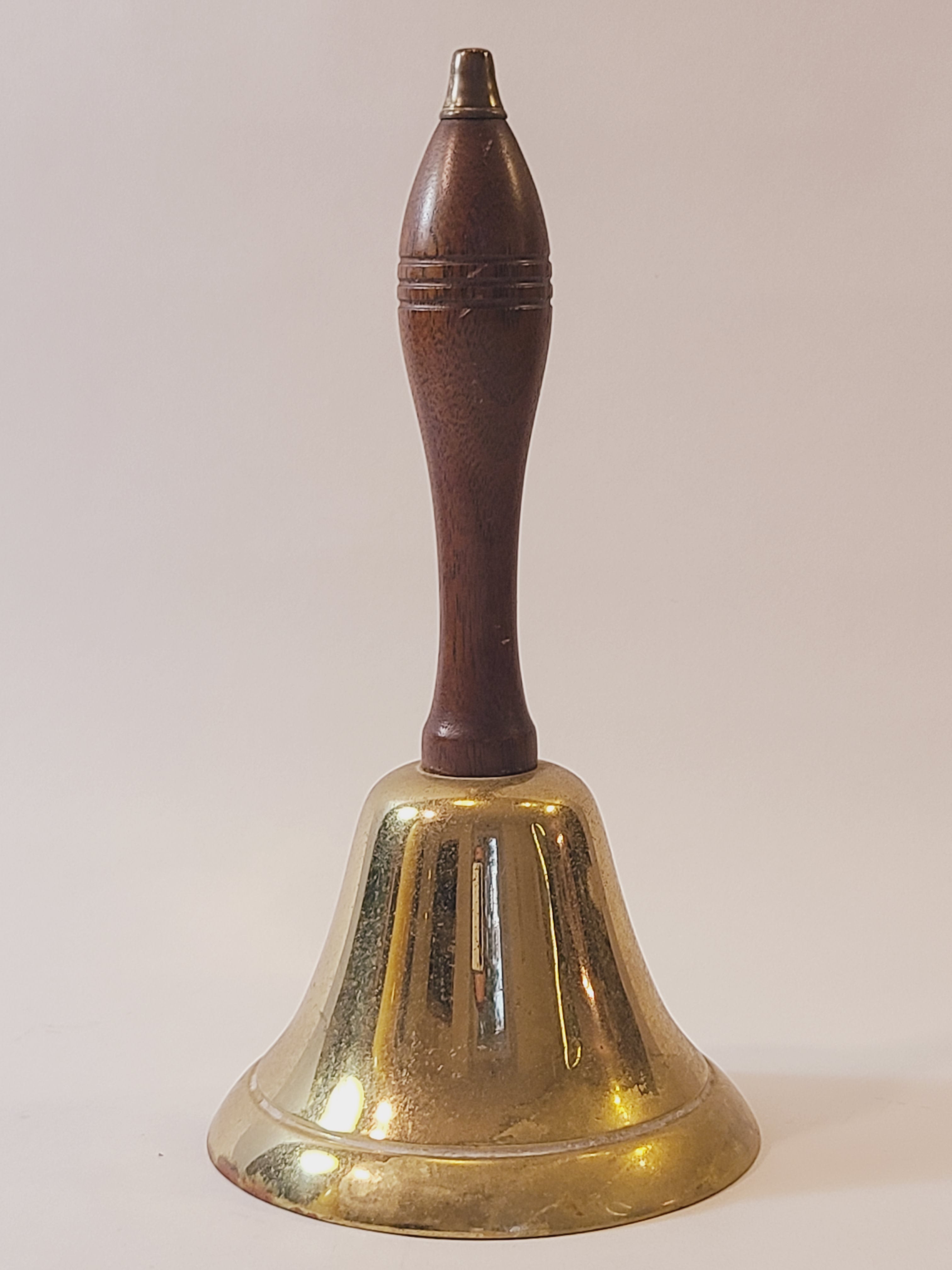 A vintage brass bell with a dark brown wooden handle, shown against a plain off-white background.