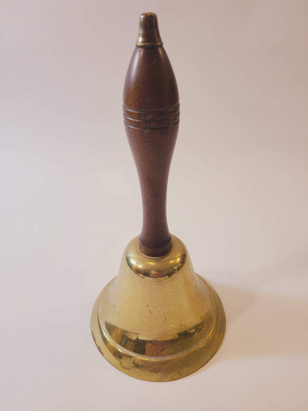 Vintage brass bell with a polished brass circular backplate and a dark brown wooden spool handle, shown against a plain off-white background.