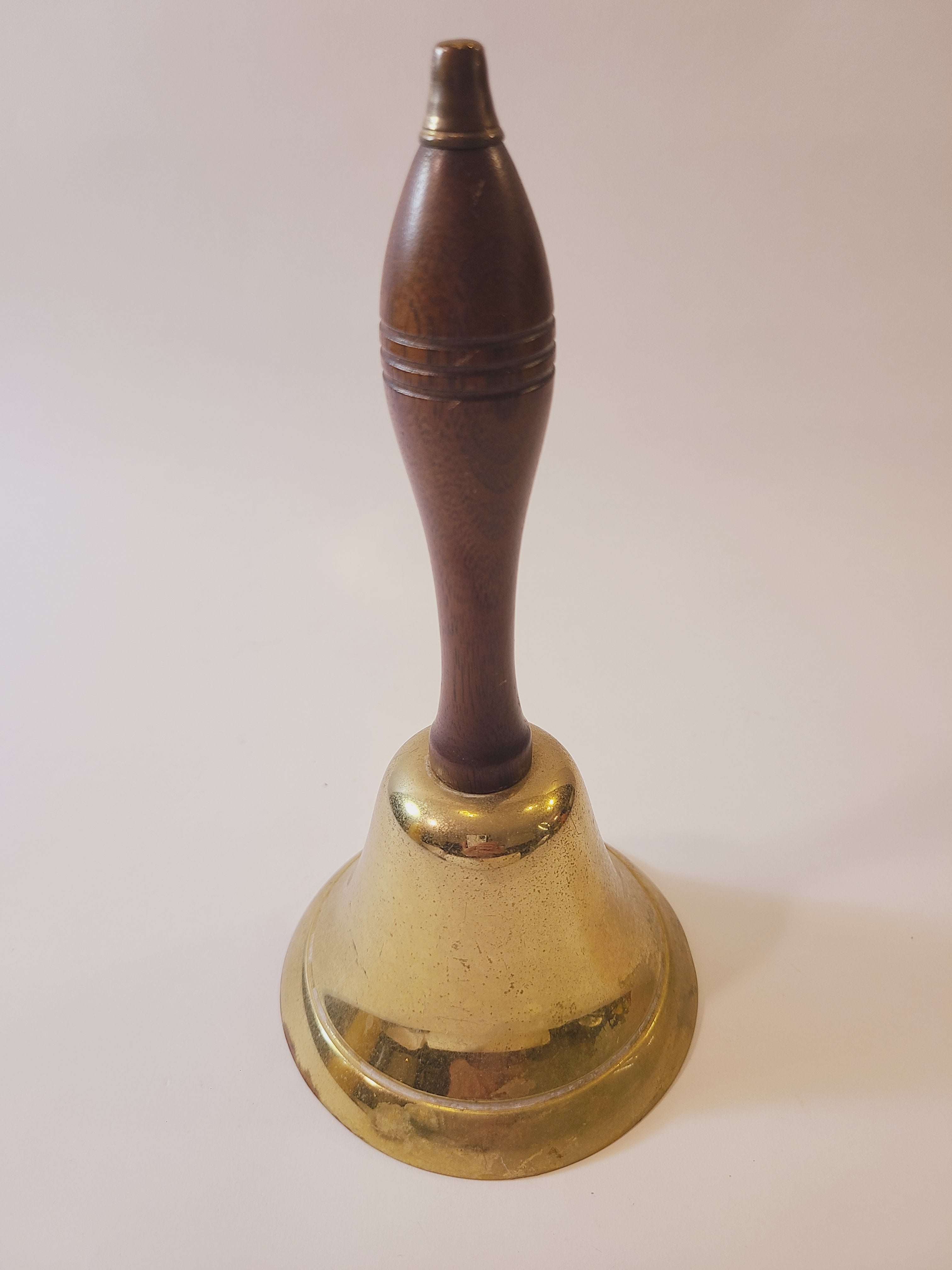 Vintage brass bell with a polished brass circular backplate and a dark brown wooden spool handle, shown against a plain off-white background.