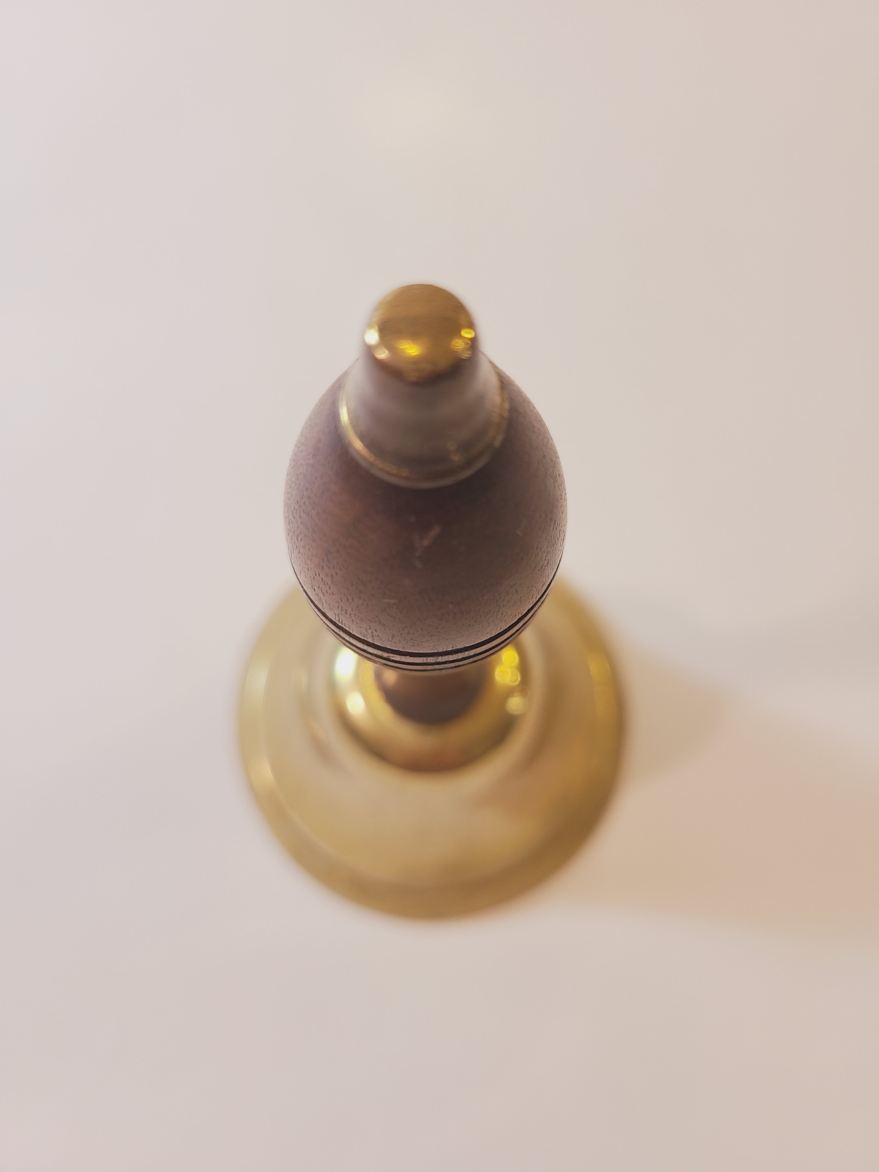 A close-up, top-down view of wood handle of vintage brass bell. 