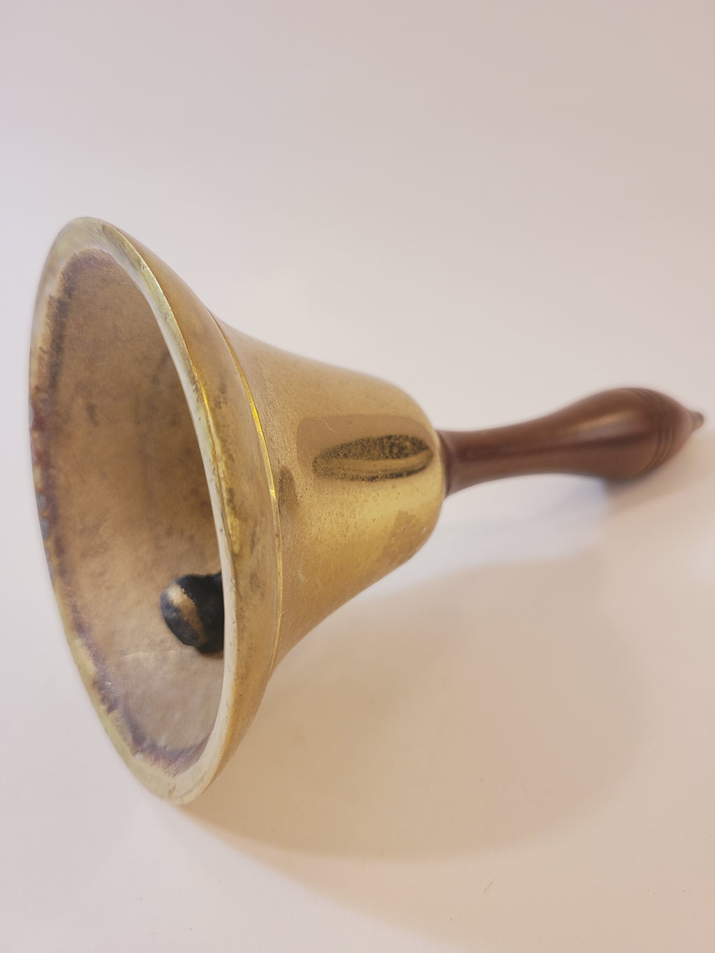 Vintage brass bell with wooden handle photographed from the side.