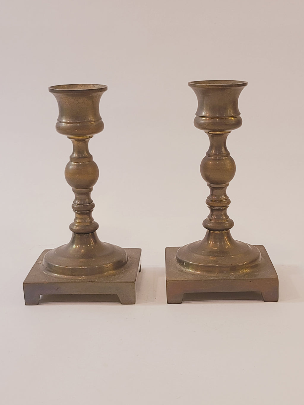 A pair of vintage brass candle holders with square bases, shown vertically against a plain off-white background.