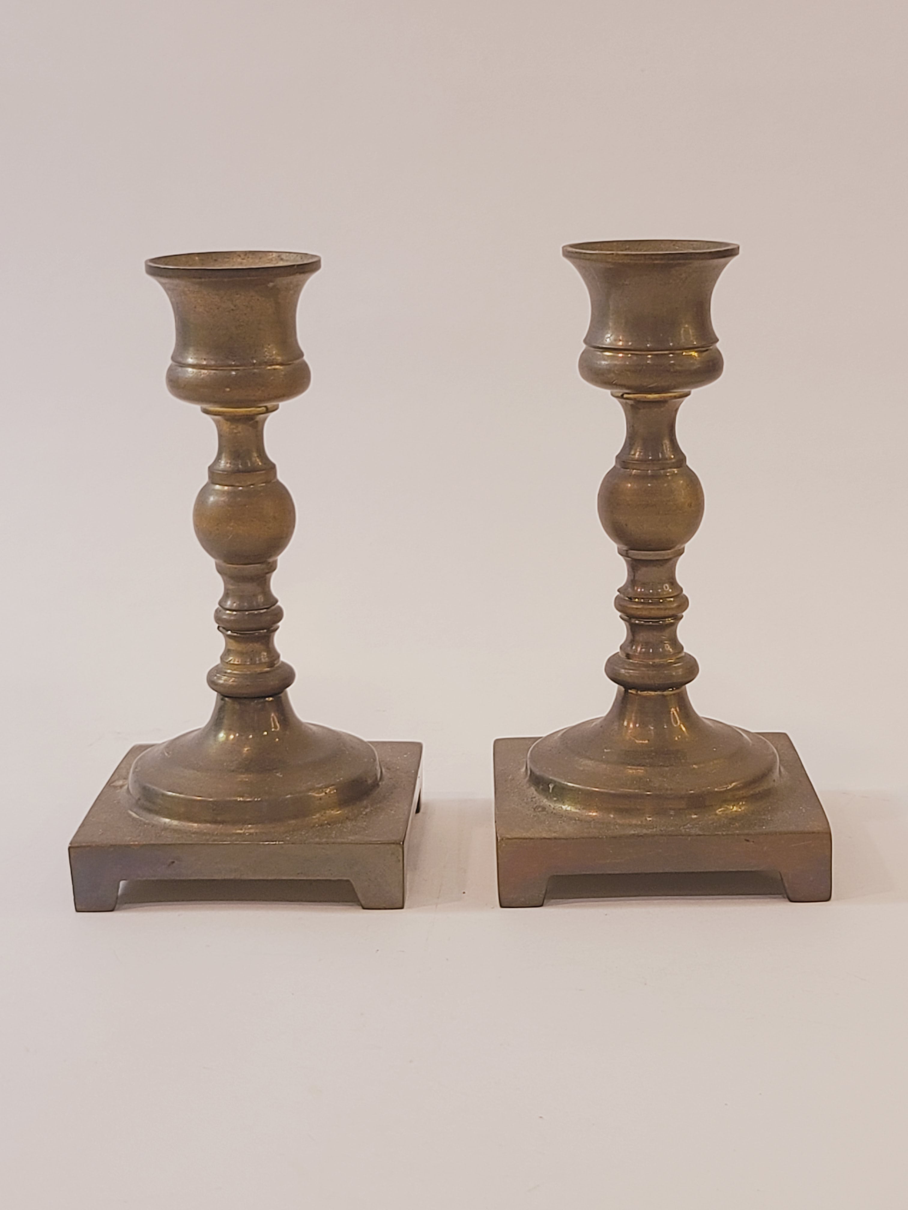 A pair of vintage brass candle holders with square bases, shown vertically against a plain off-white background.