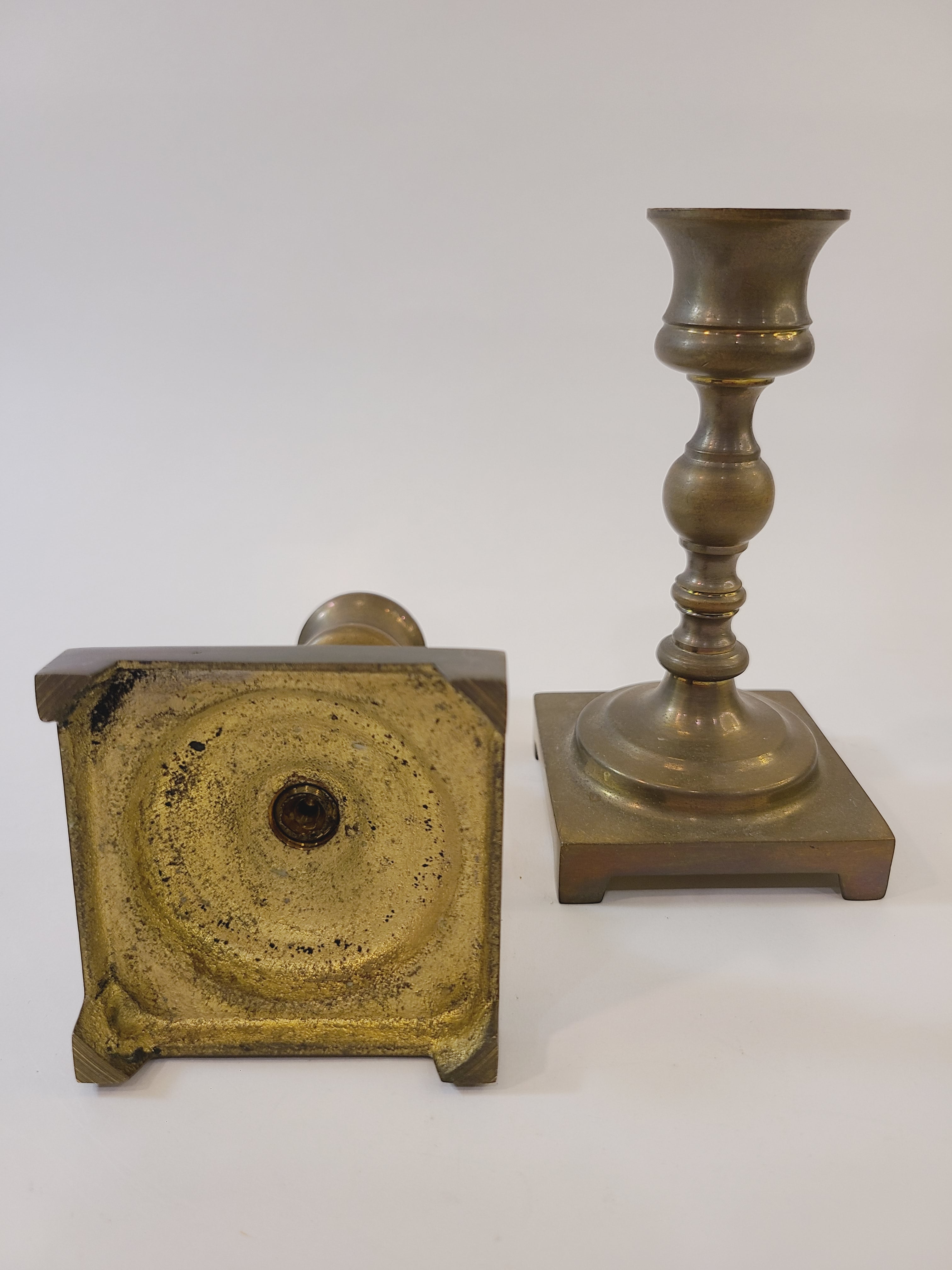 A pair of vintage brass candle holders with square bases photographed to show the base of one.
