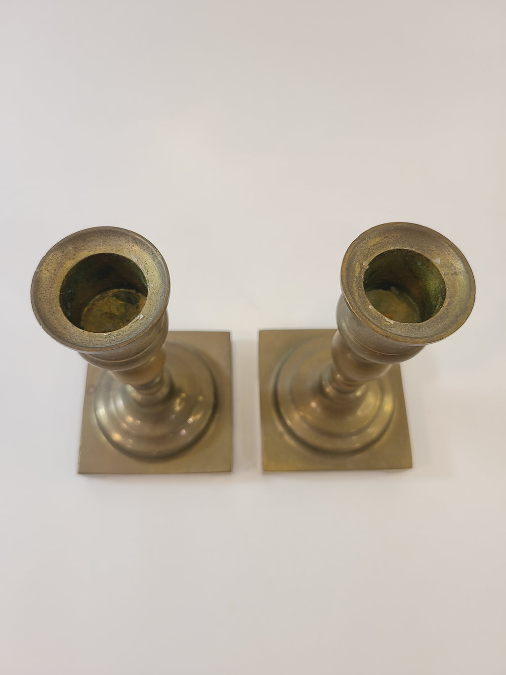 A pair of vintage brass candle holders with square bases, shown from above.