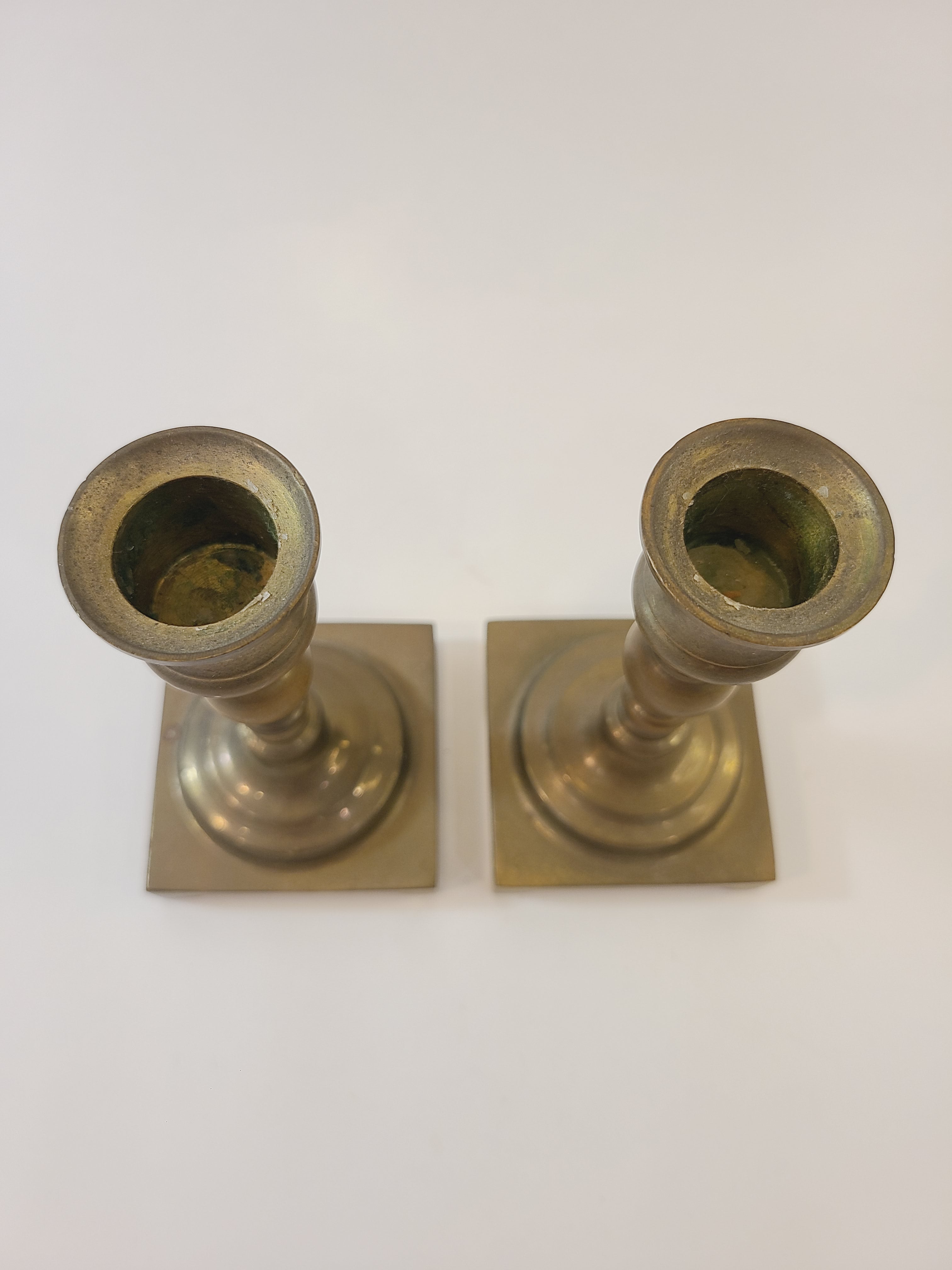 A pair of vintage brass candle holders with square bases, shown from above.