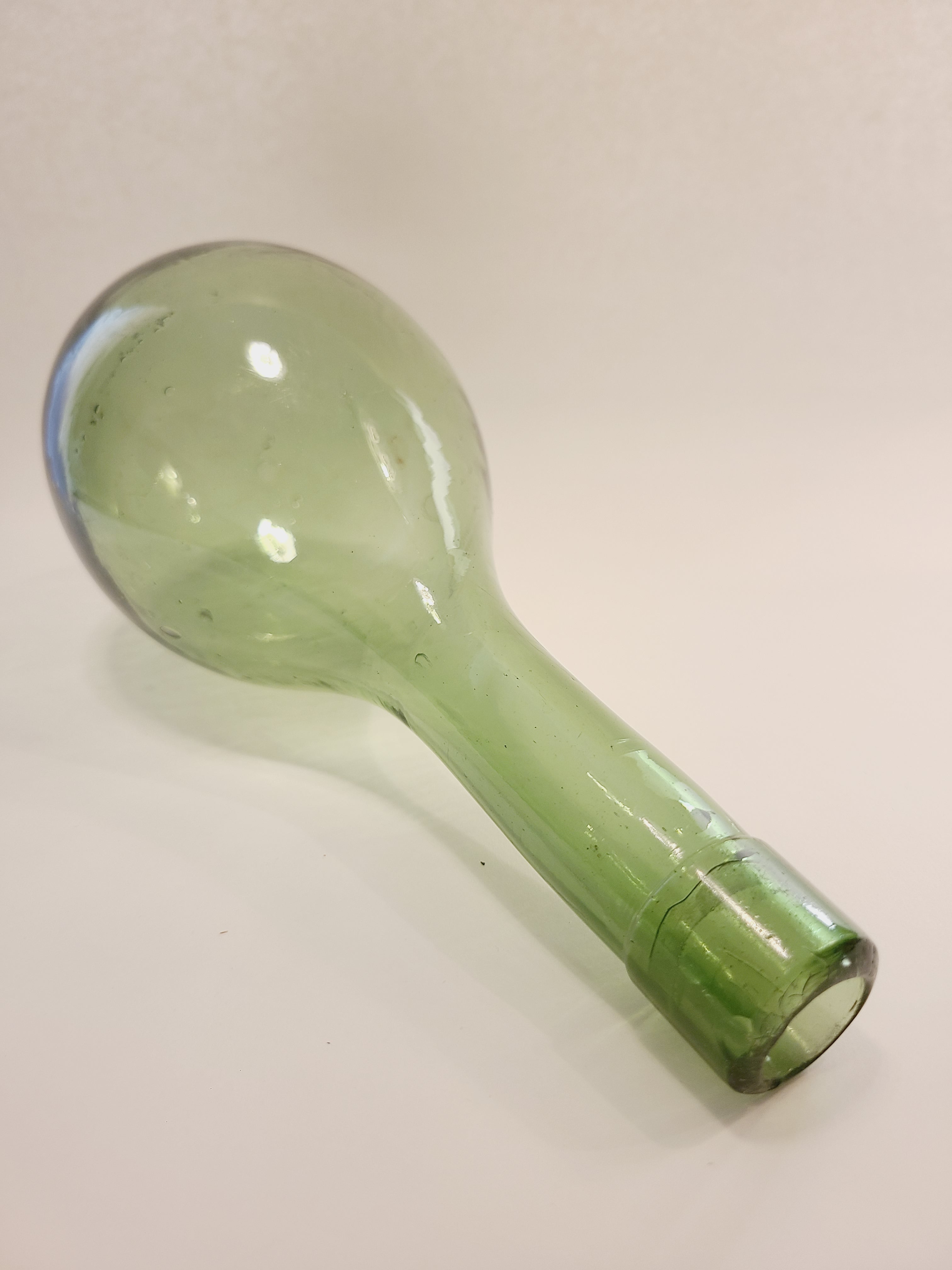 A vintage light green glass bottle with a bulbous round bottom and a narrow neck, shown on a plain off-white background.
