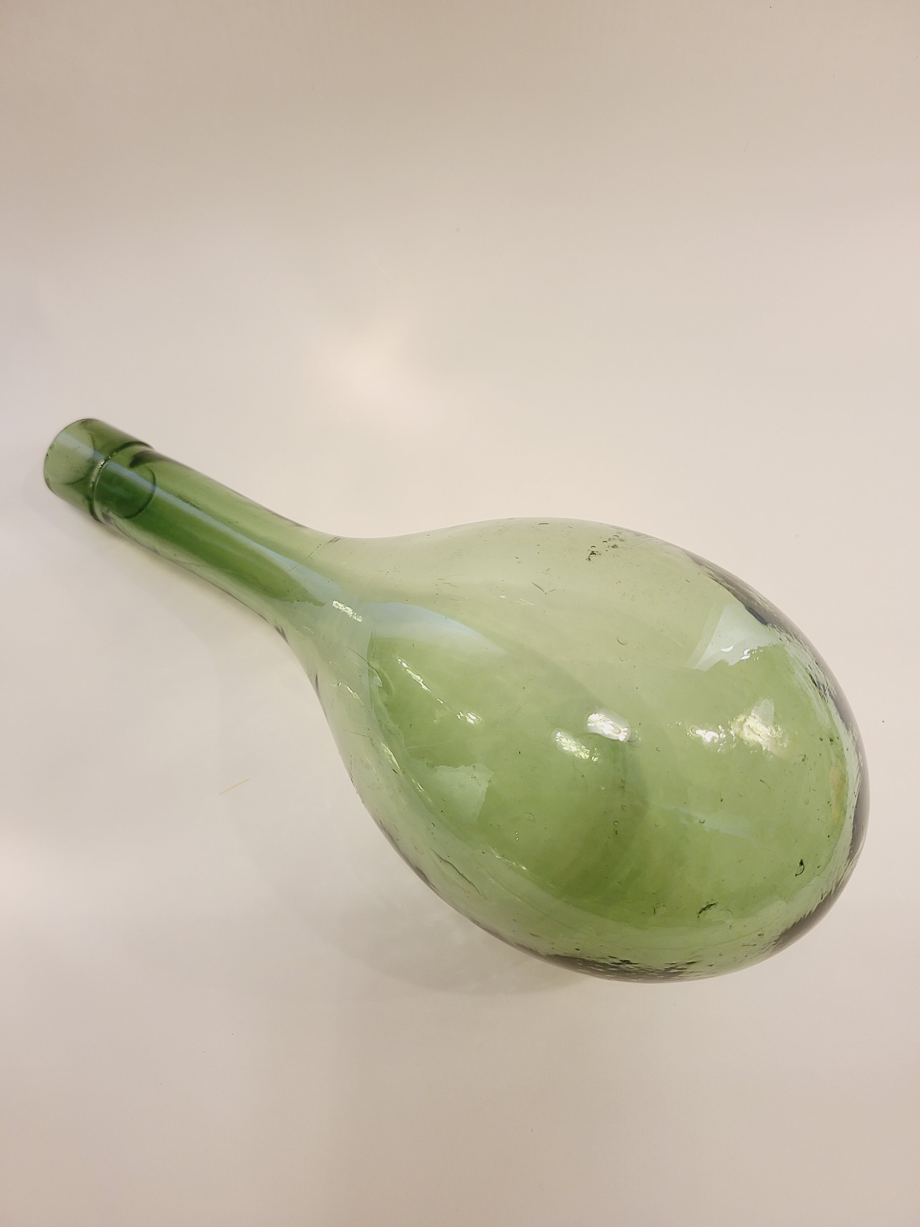 A vintage green glass bottle with a round bottom shown on a plain off-white background.