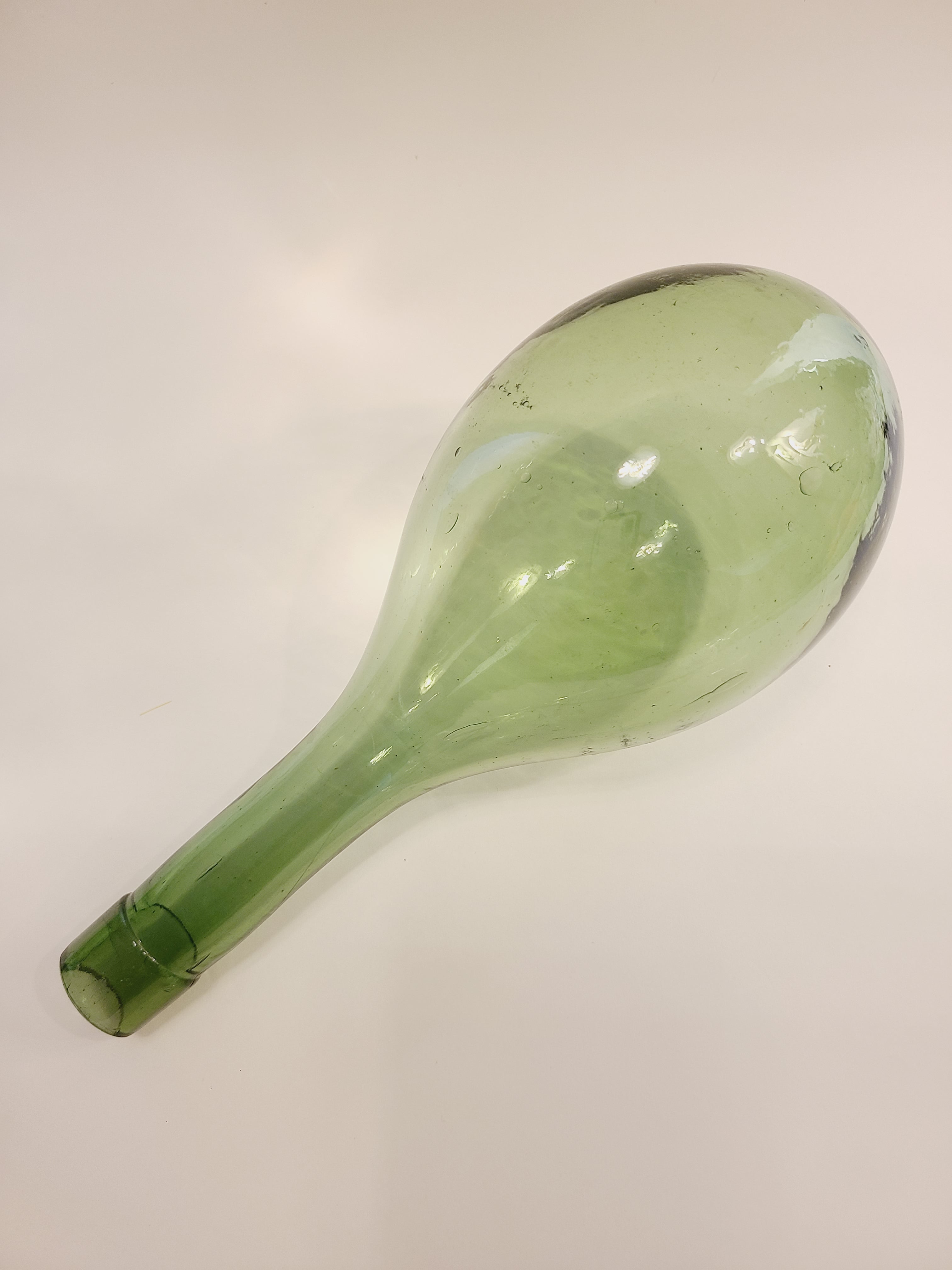 A vintage green glass bottle with a bulbous body and a long neck, shown diagonally on a plain off-white background.