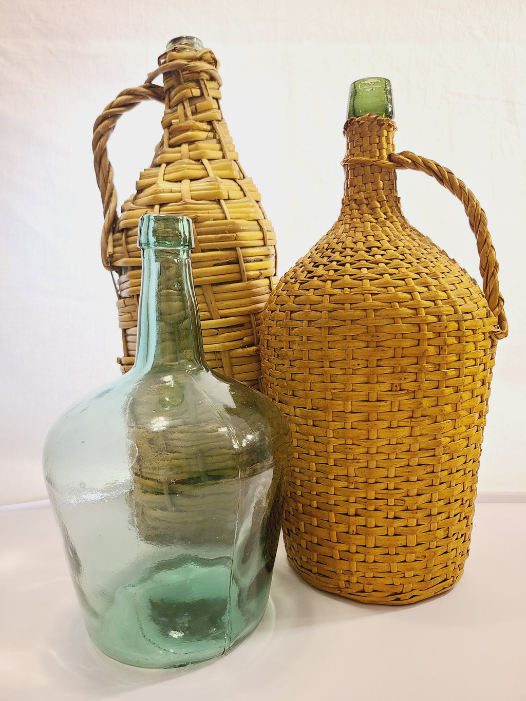 Vintage demijohn green glass with original rattan wrapping displayed with other demijohns.
