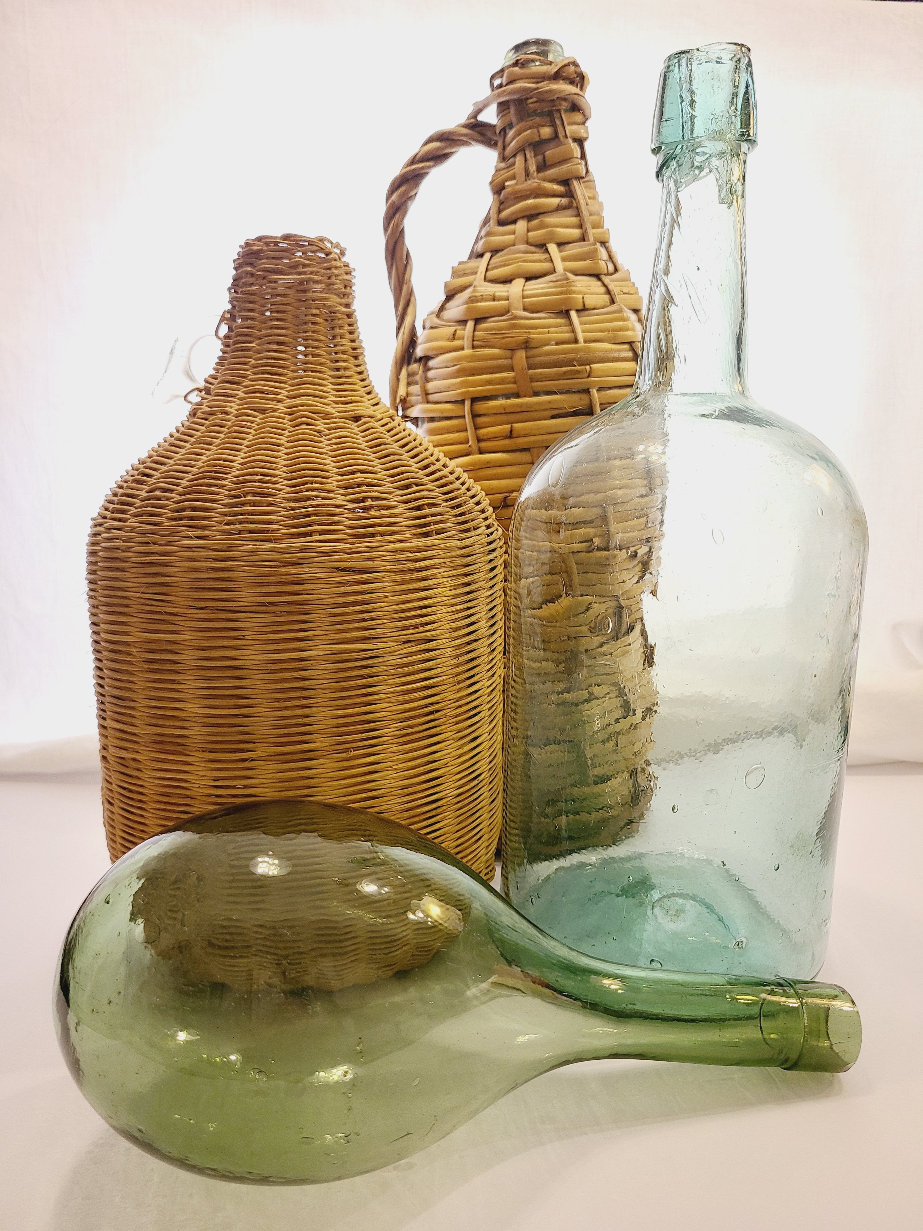 Vintage green glass round bottom bottle displayed with vintage demijohns.