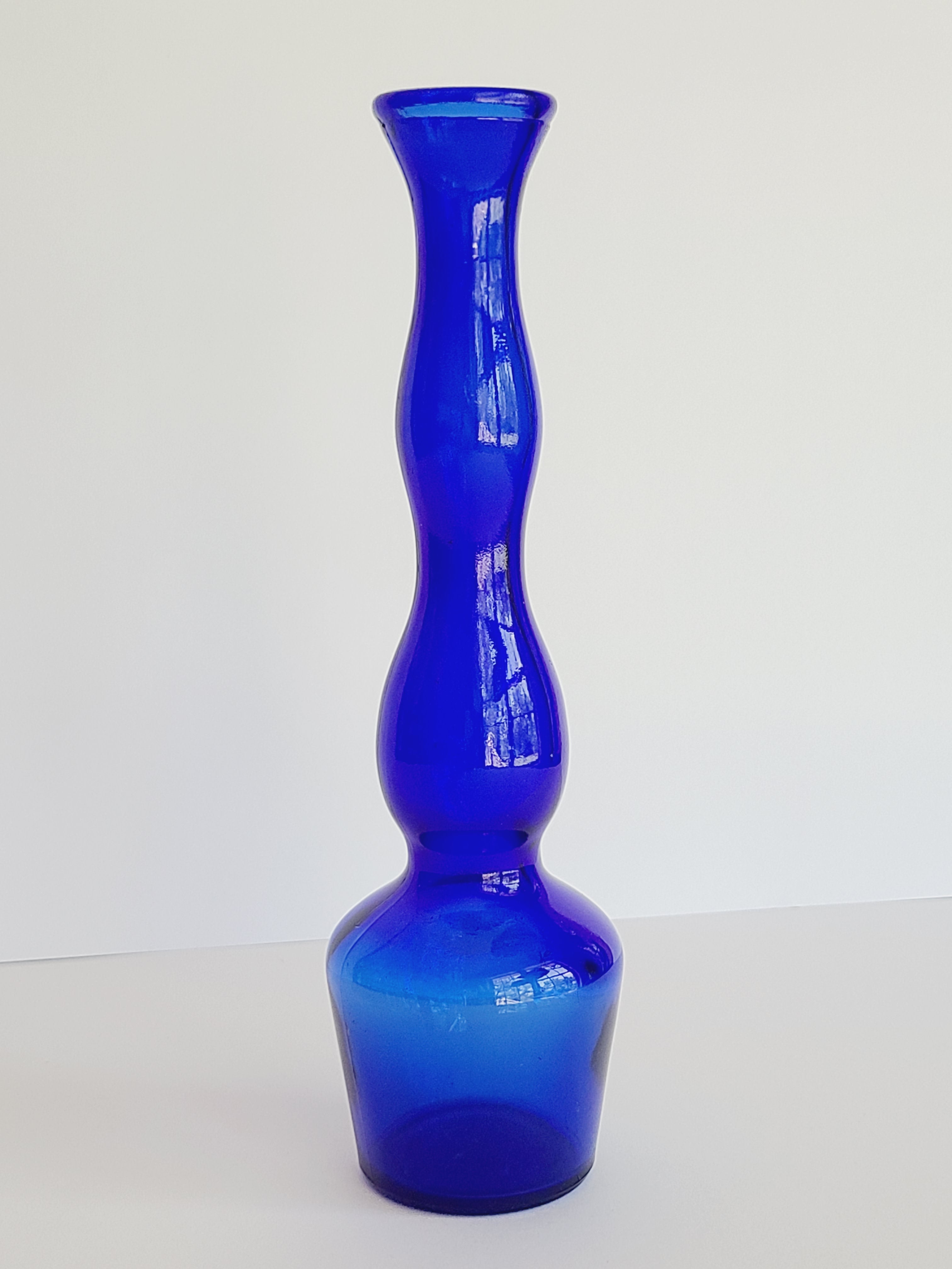 A vintage cobalt blue glass bud vase with an hourglass-like silhouette on a plain white background.