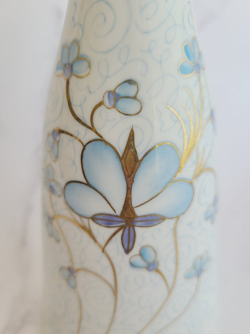 Close up of Andrea by Sadek vintage white porcelain vase made in Japan hand-painted with light blue floral motifs, gold accents, and a blue-and-gold patterned band at the neck. 