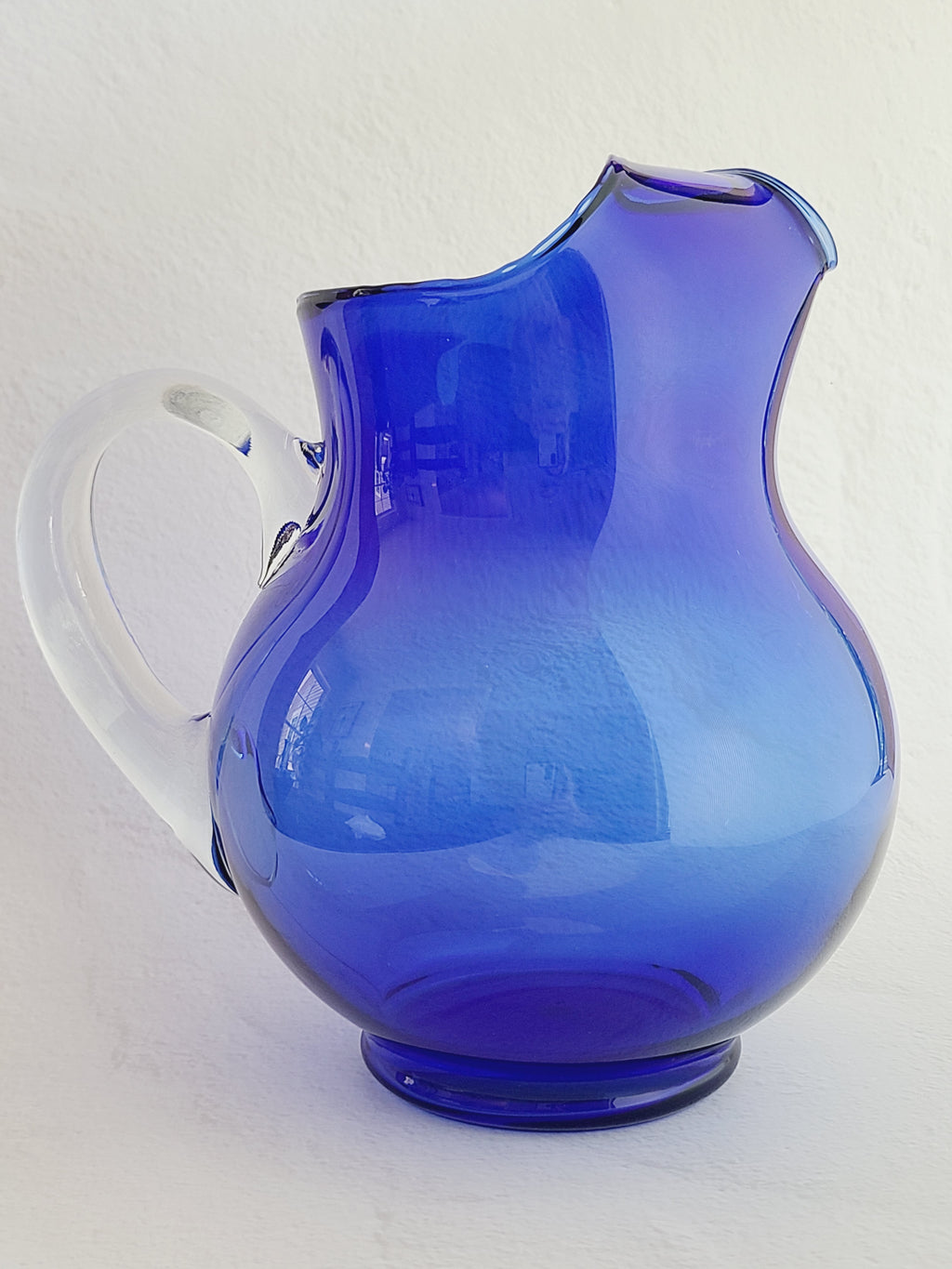 A vintage cobalt blue glass pitcher with a clear glass handle, shown from the side.