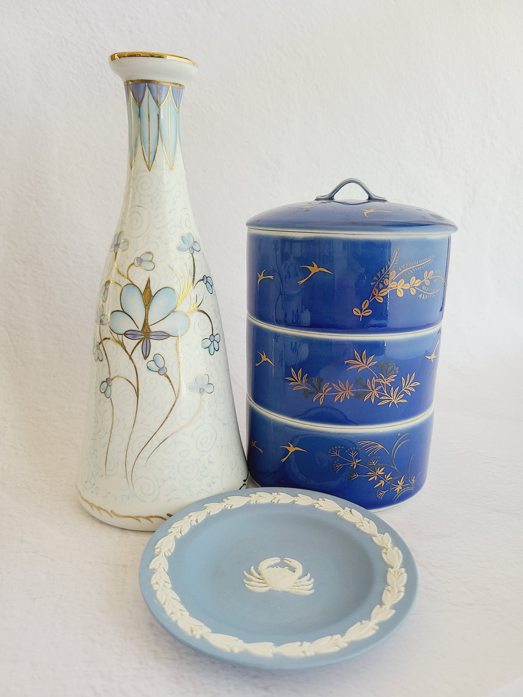 Andrea by Sadek vintage white porcelain vase made in Japan hand-painted with light blue floral motifs, gold accents, and a blue-and-gold patterned band at the neck displayed with blue tier bowls and blue dish.