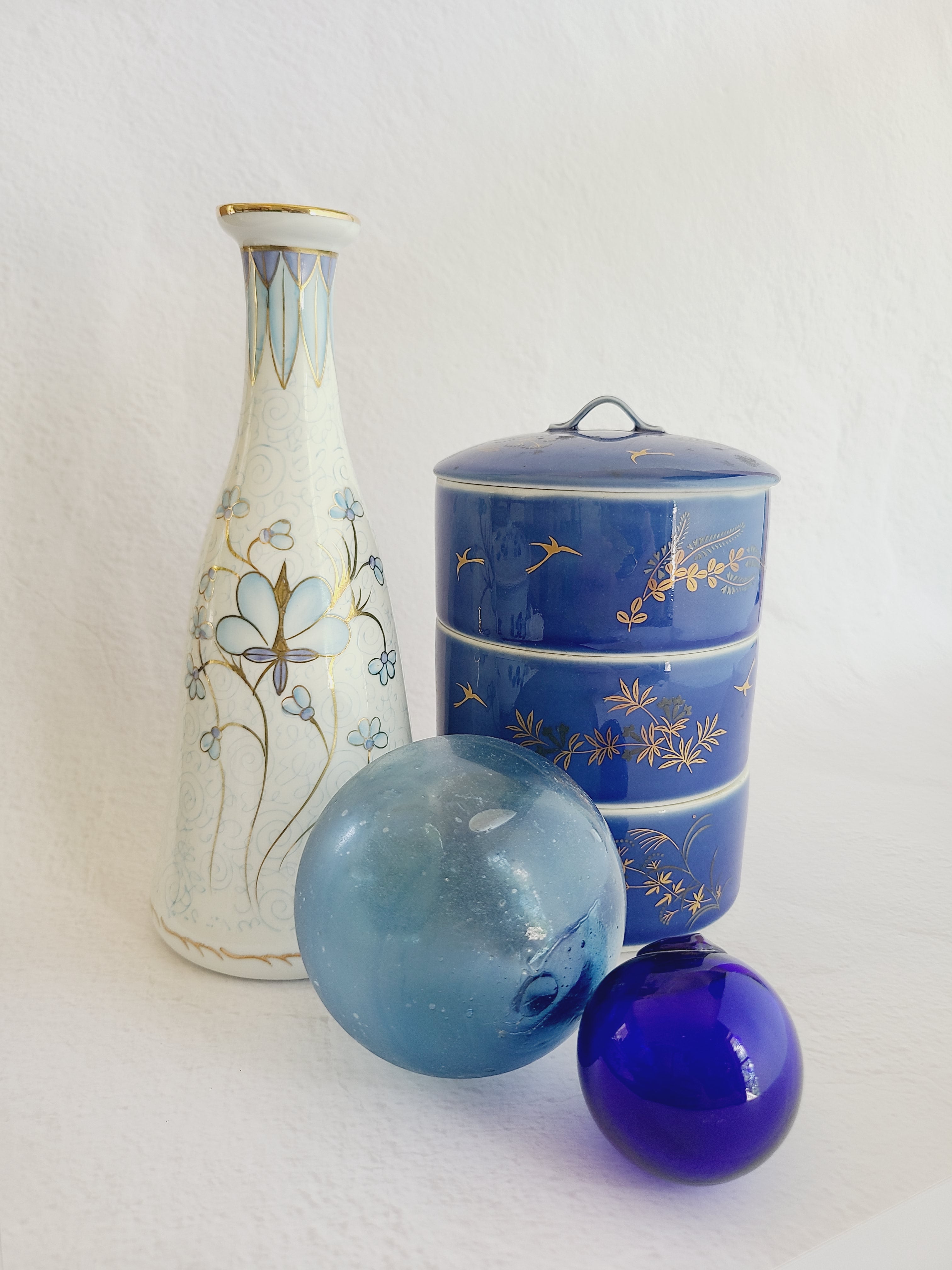 Vintage Fukagawa Seiji 3-Tier Stacking Bowl Set with Lid in lapis blue with gold accents displayed with glass fishing floats.