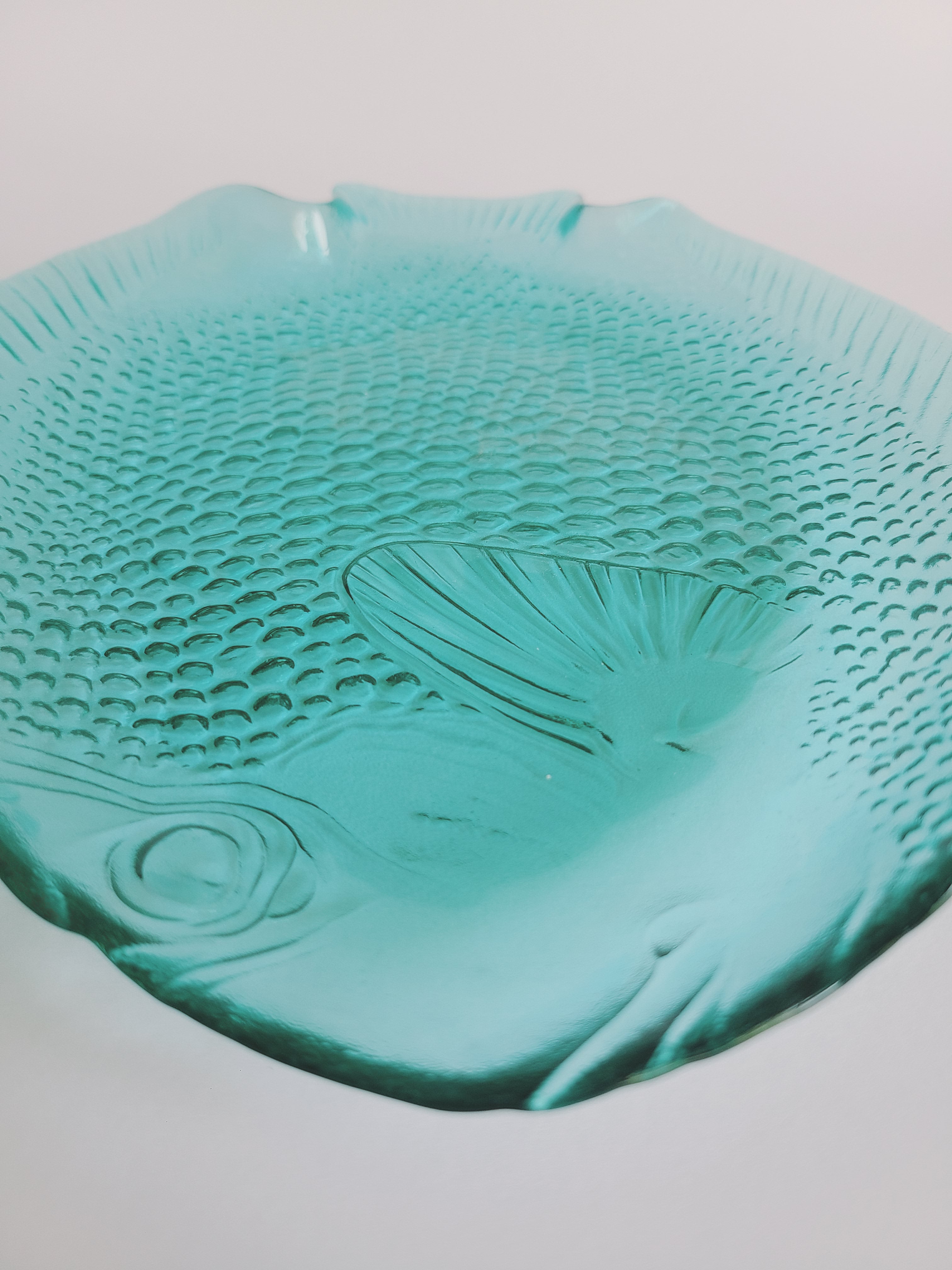 Close up of vintage Arcoroc turquoise glass plate shaped like a fish, featuring detailed embossed scales and fins made in France.