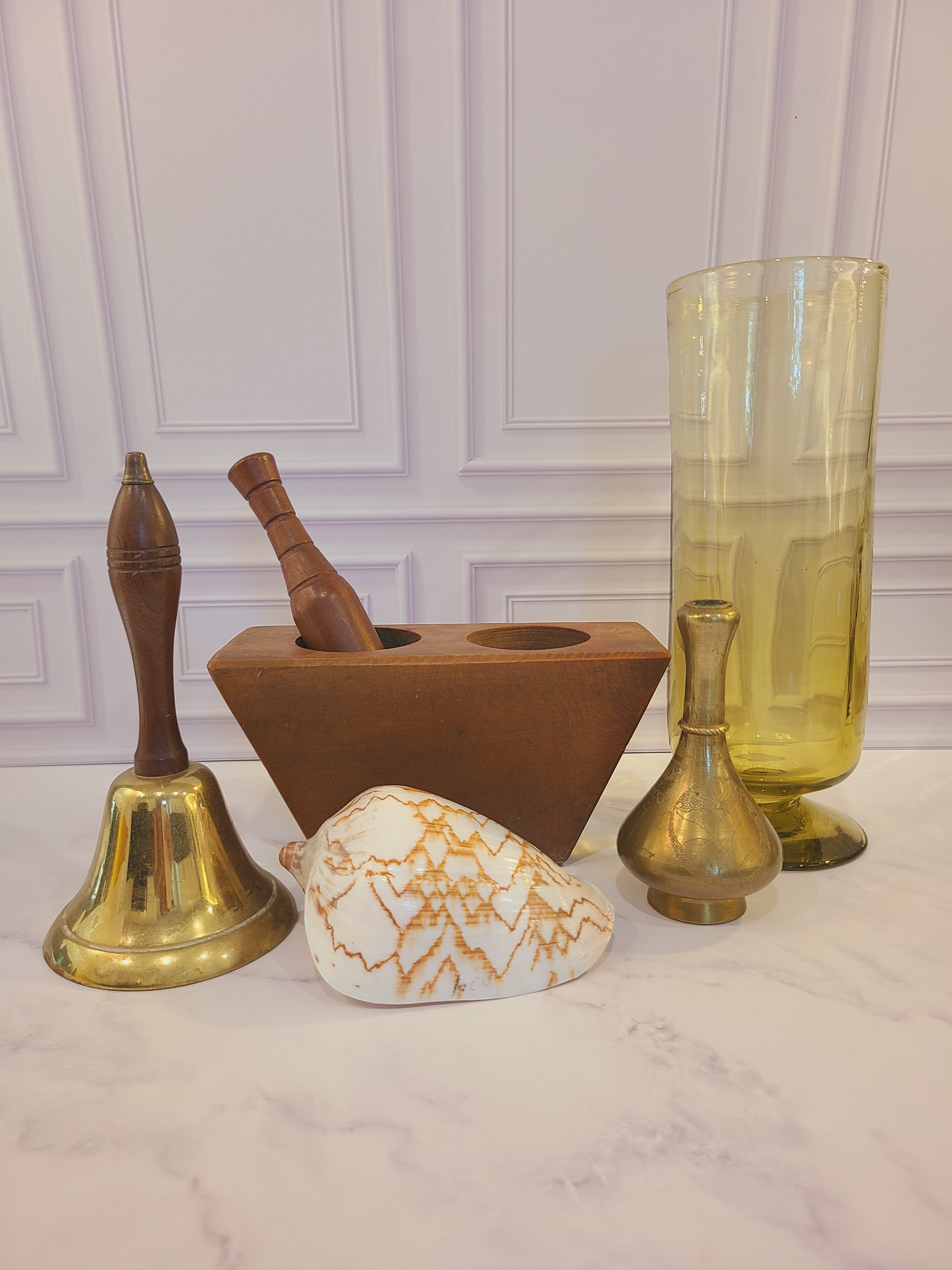 Vintage brass bell with wood handle displayed with glass vase, shell, brass vase, wood sugar mold.
