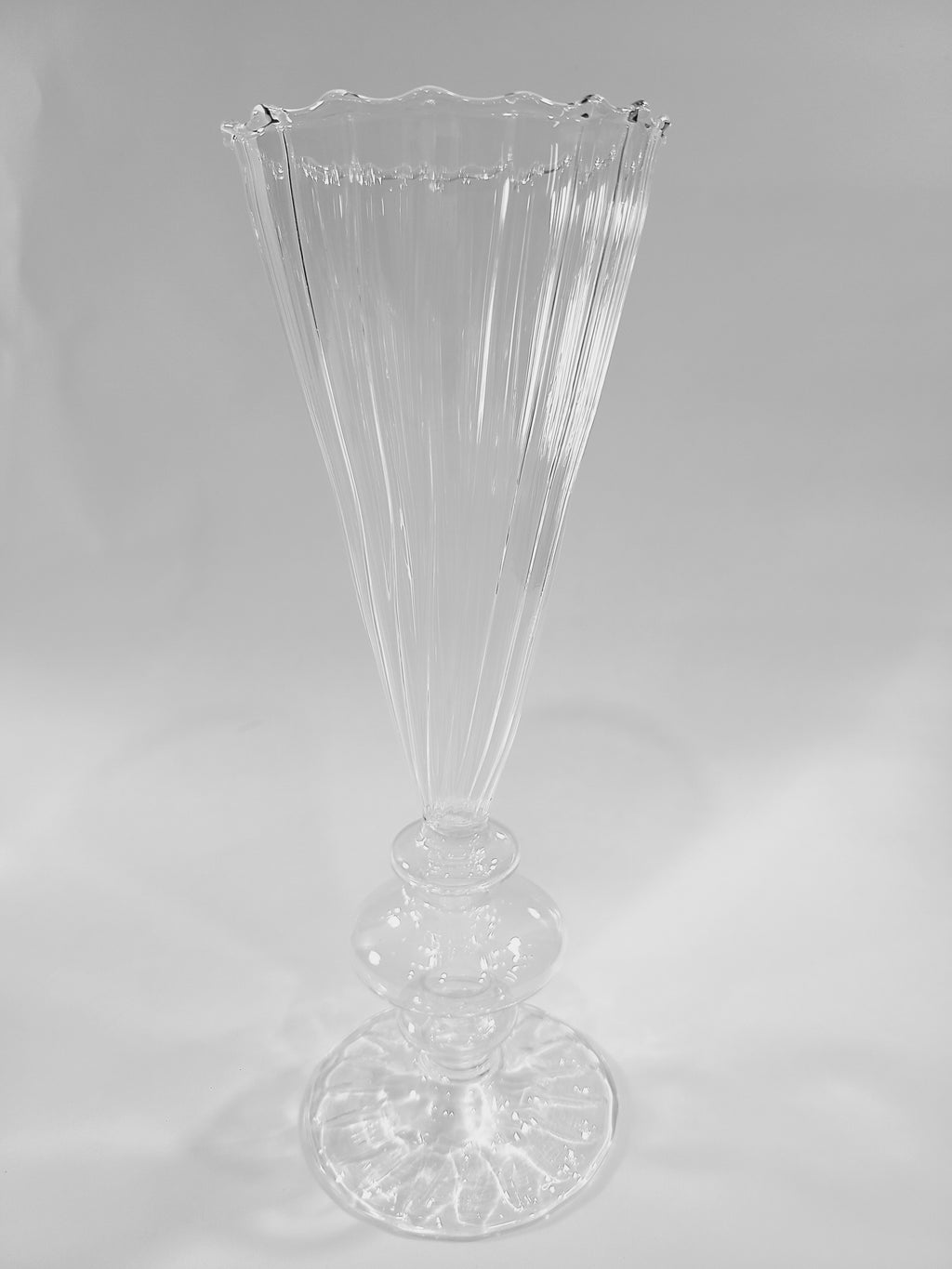 A clear ribbed glass vase with a flared, scalloped rim and a pedestal base.