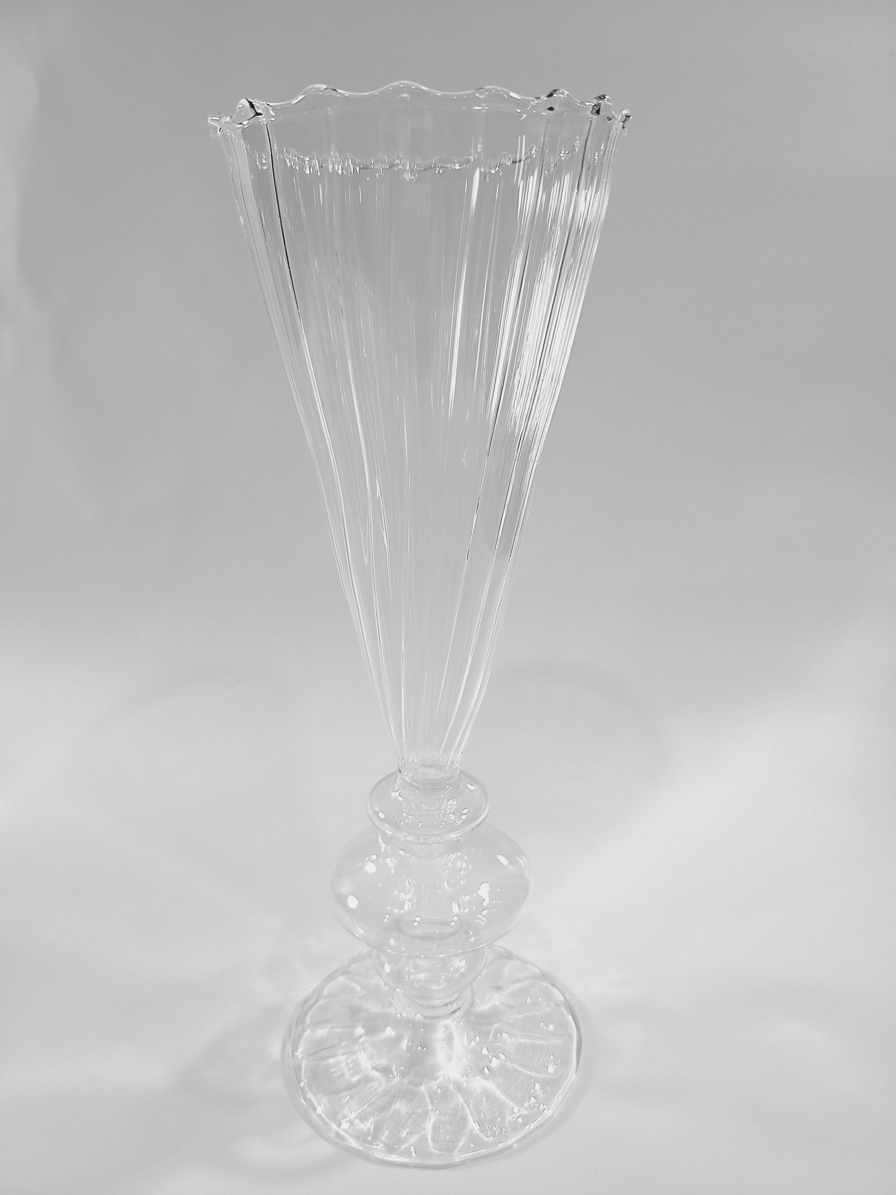 A clear ribbed glass vase with a flared, scalloped rim and a pedestal base.